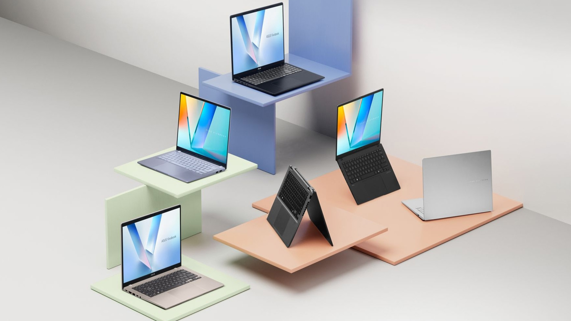 Multiple ASUS Vivobook laptops showcased across pastel colored tiered display platforms.