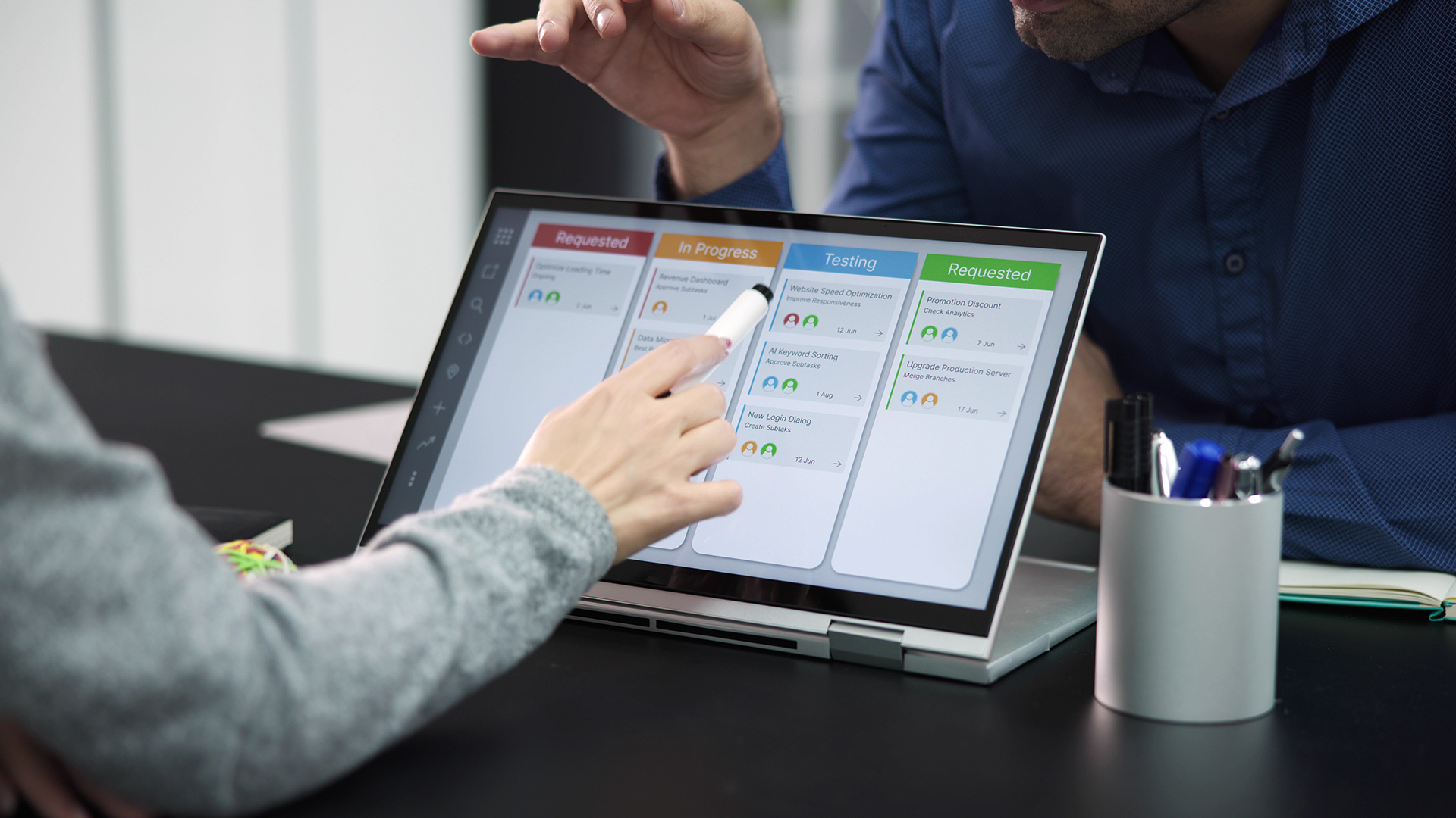 Business professionals collaborating on a 2-in-1 convertible laptop touchscreen during a meeting.