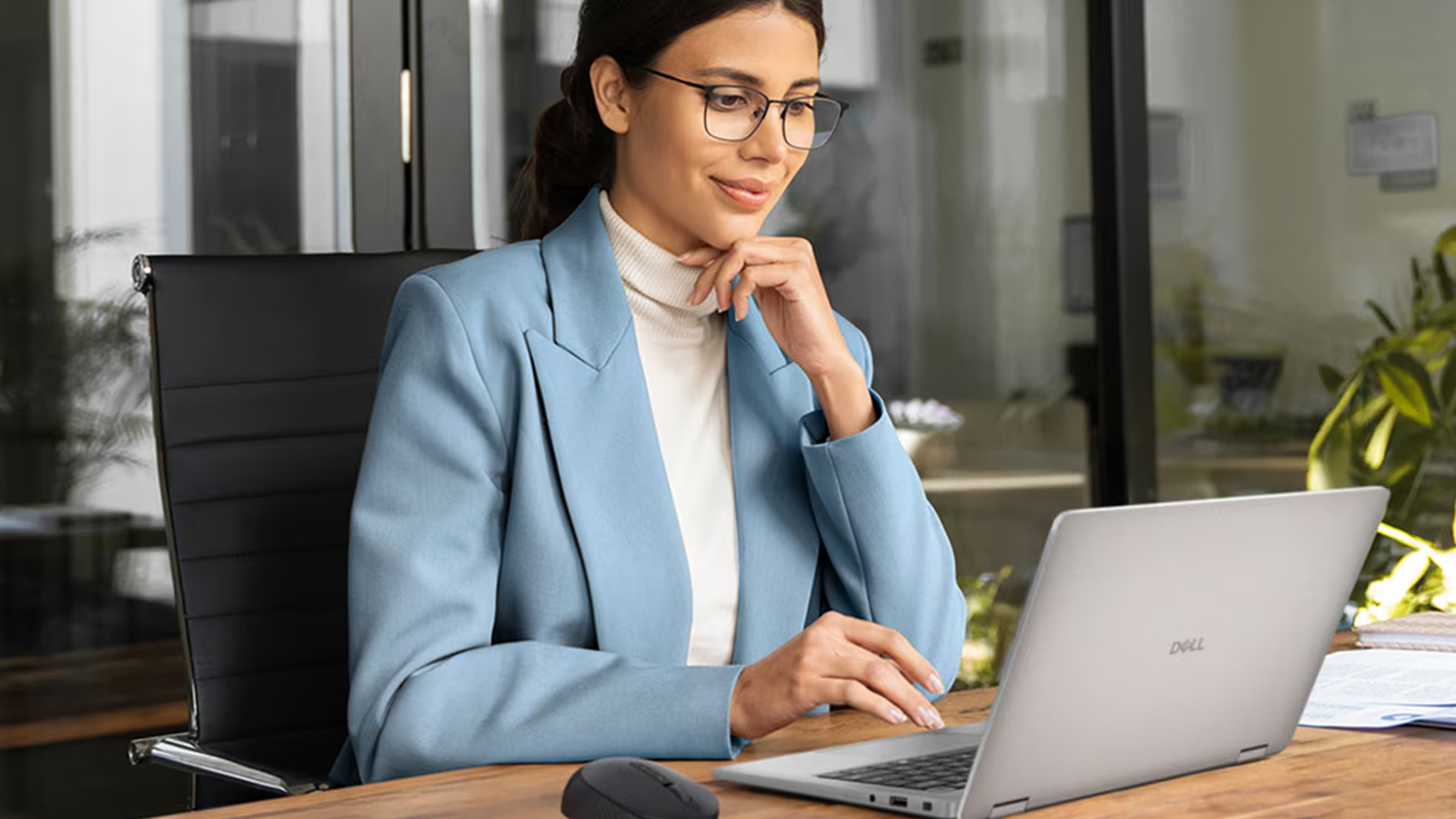 tudent in a blue blazer working on a silver Dell laptop at a desk.