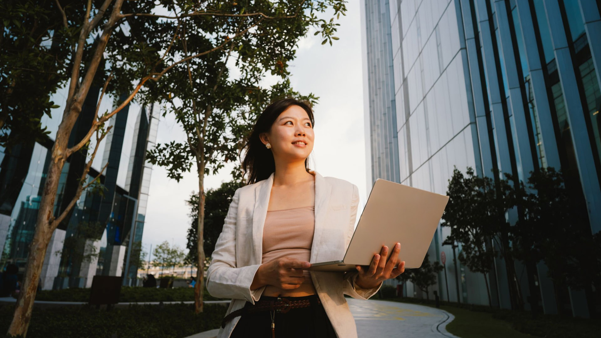 Woman holding a lightweight laptop outdoors near modern office buildings.