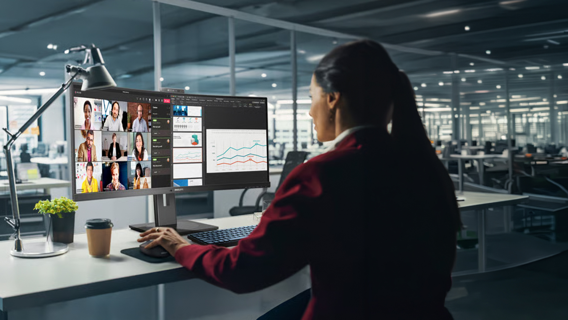 Businesswoman using a large Philips monitor for a video call and data charts.