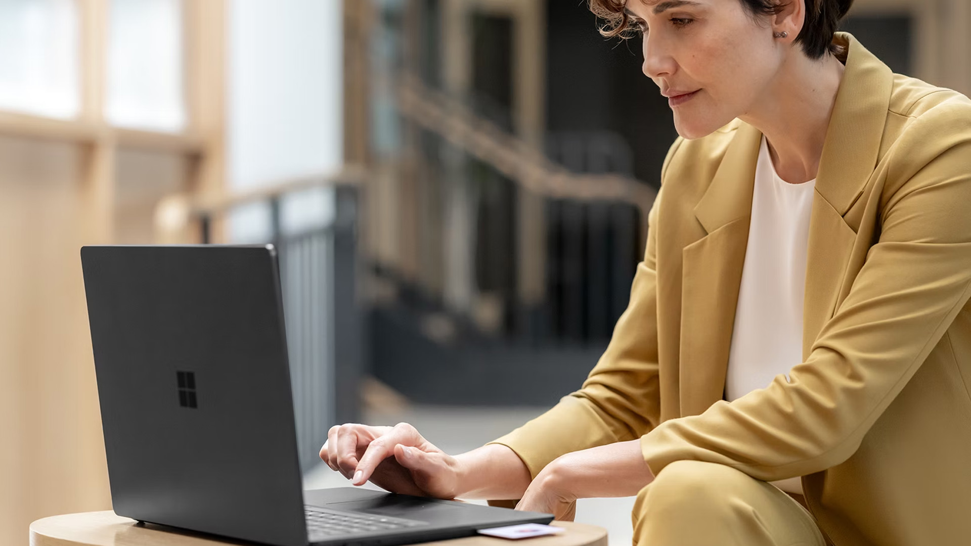 A professional businesswoman working on a black Microsoft Surface laptop in an office.