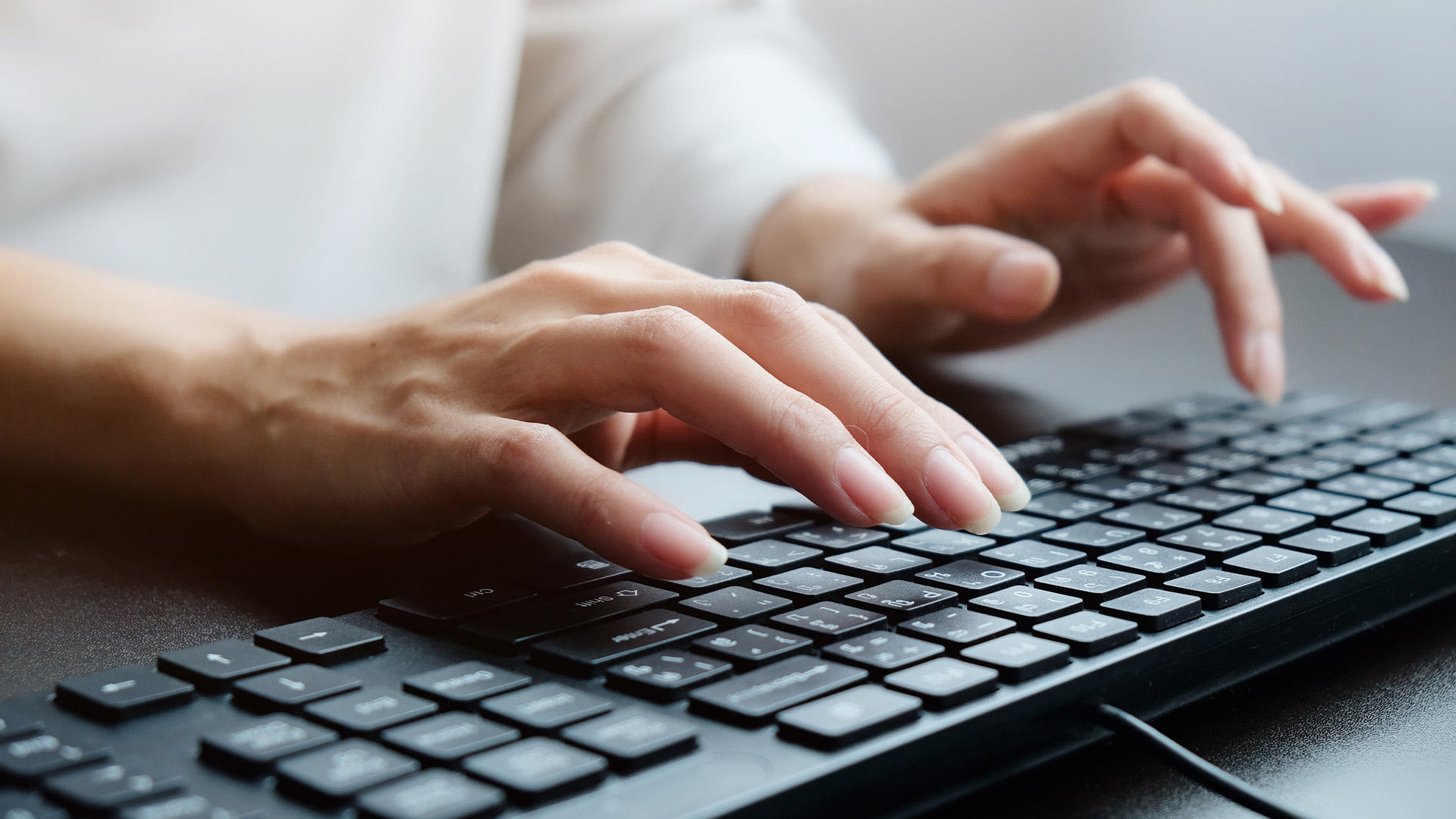 Close-up view of a person's hands typing on a black desktop computer keyboard.