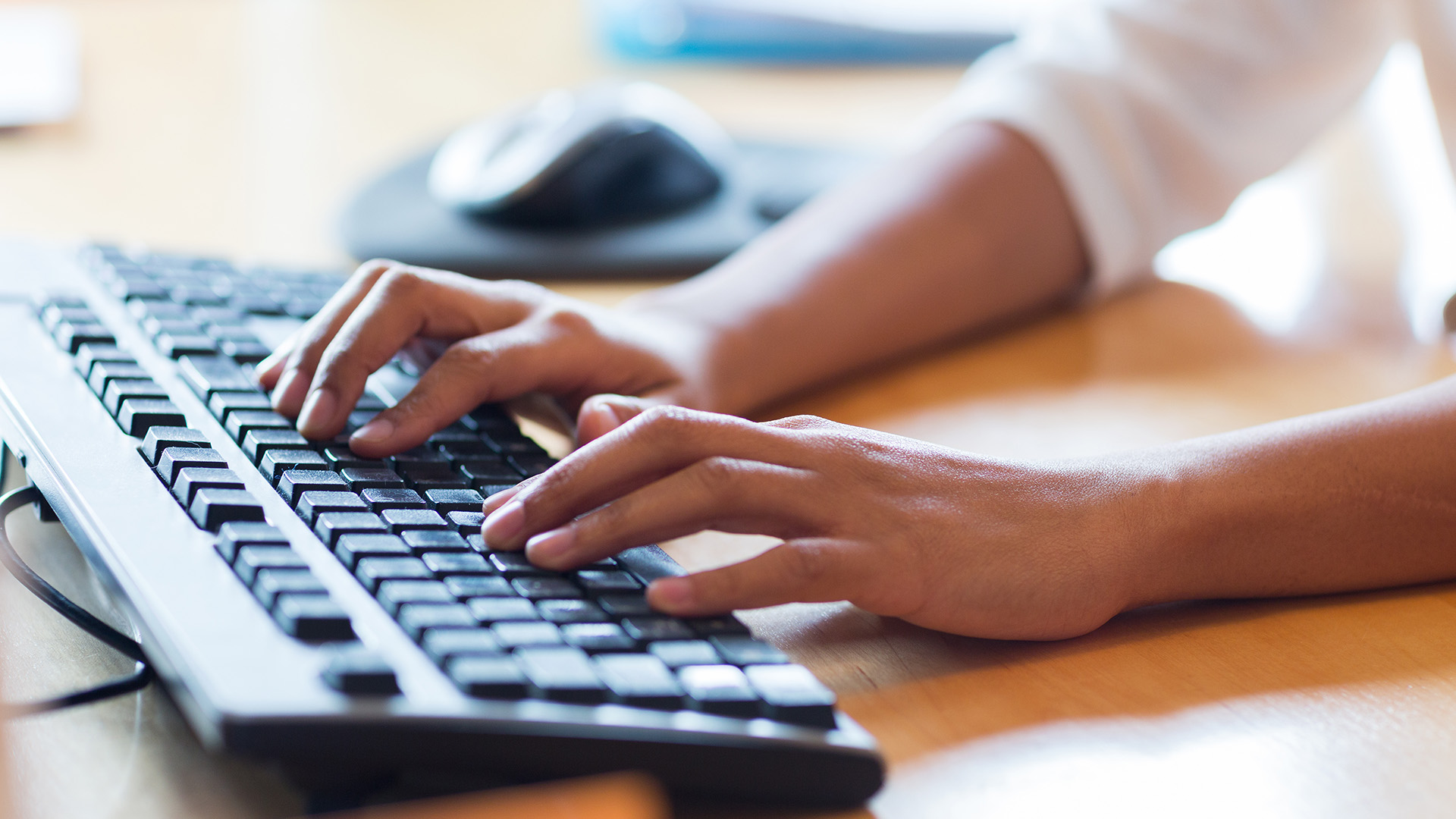 Close-up of hands typing on a desktop keyboard.