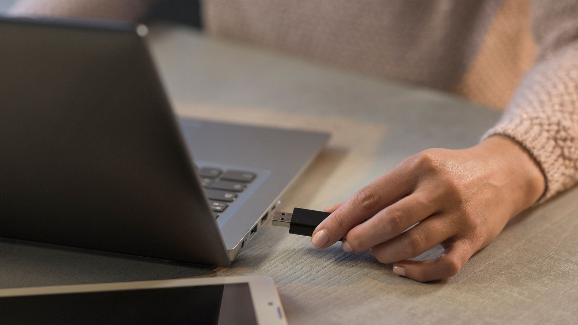 Close-up view of a hand plugging a black USB flash drive into a laptop port.