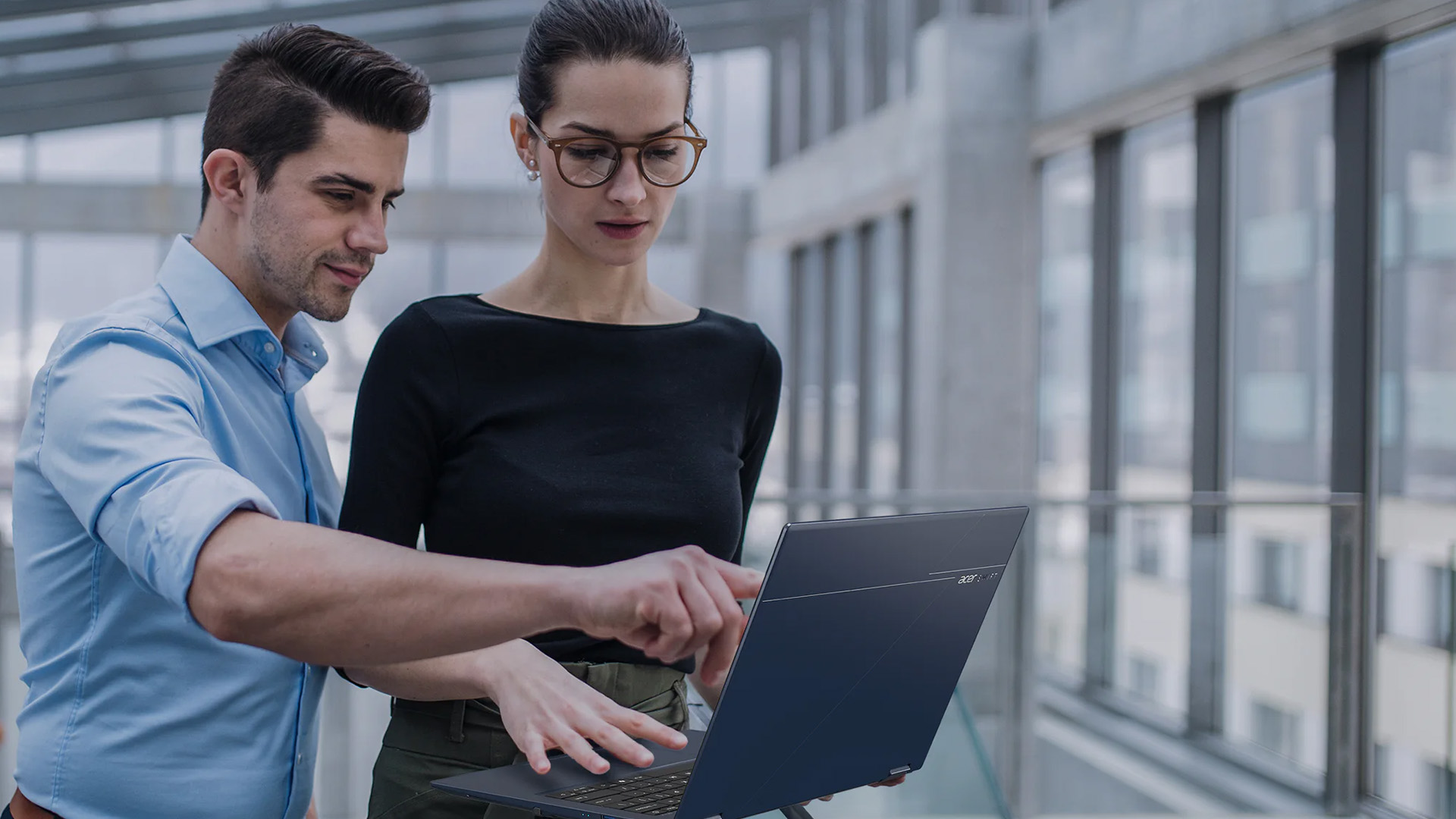 Two colleagues in a modern office looking at and pointing to a blue Acer laptop.