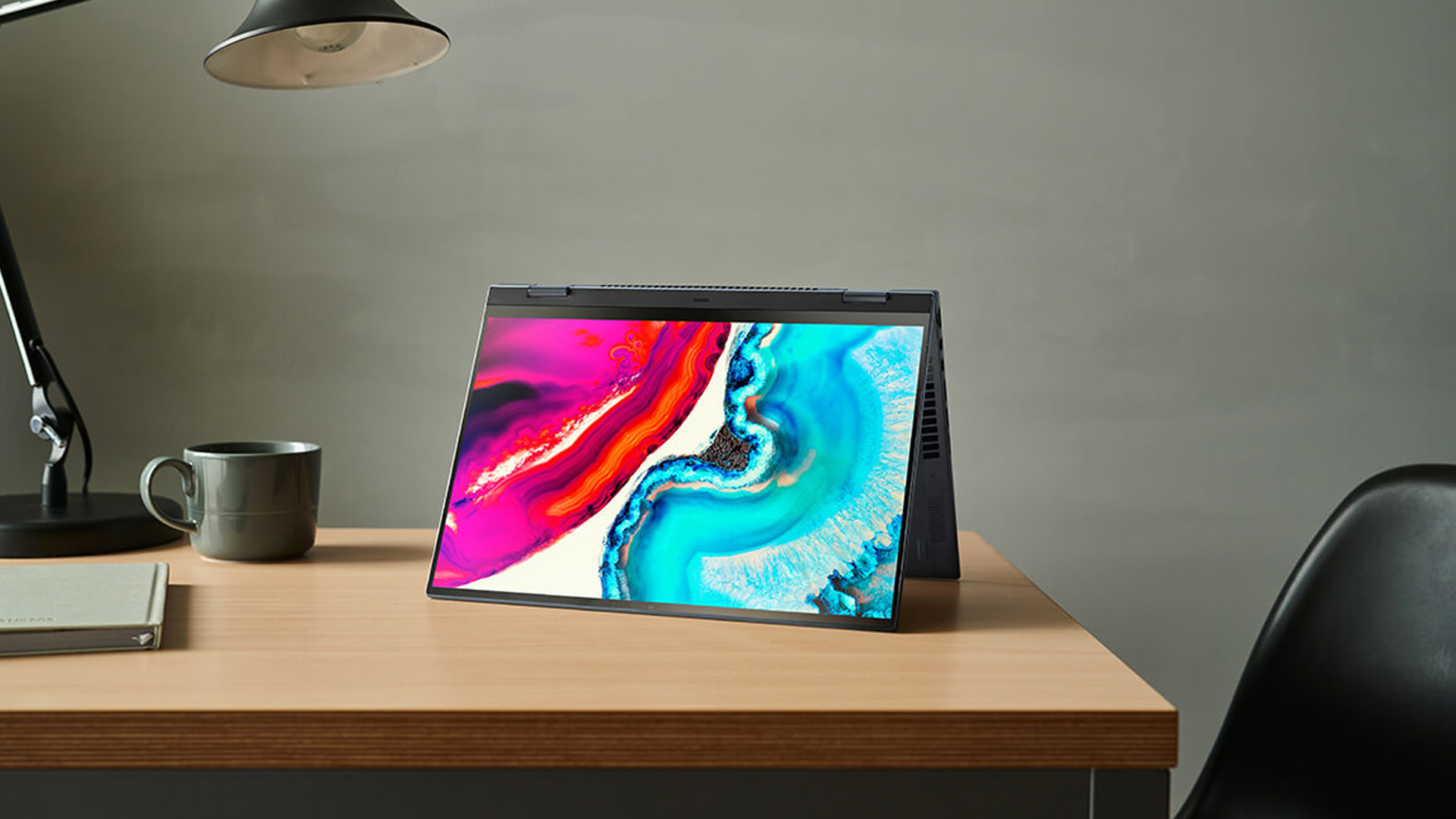 Convertible OLED laptop in tent mode displaying vibrant abstract art on a desk.