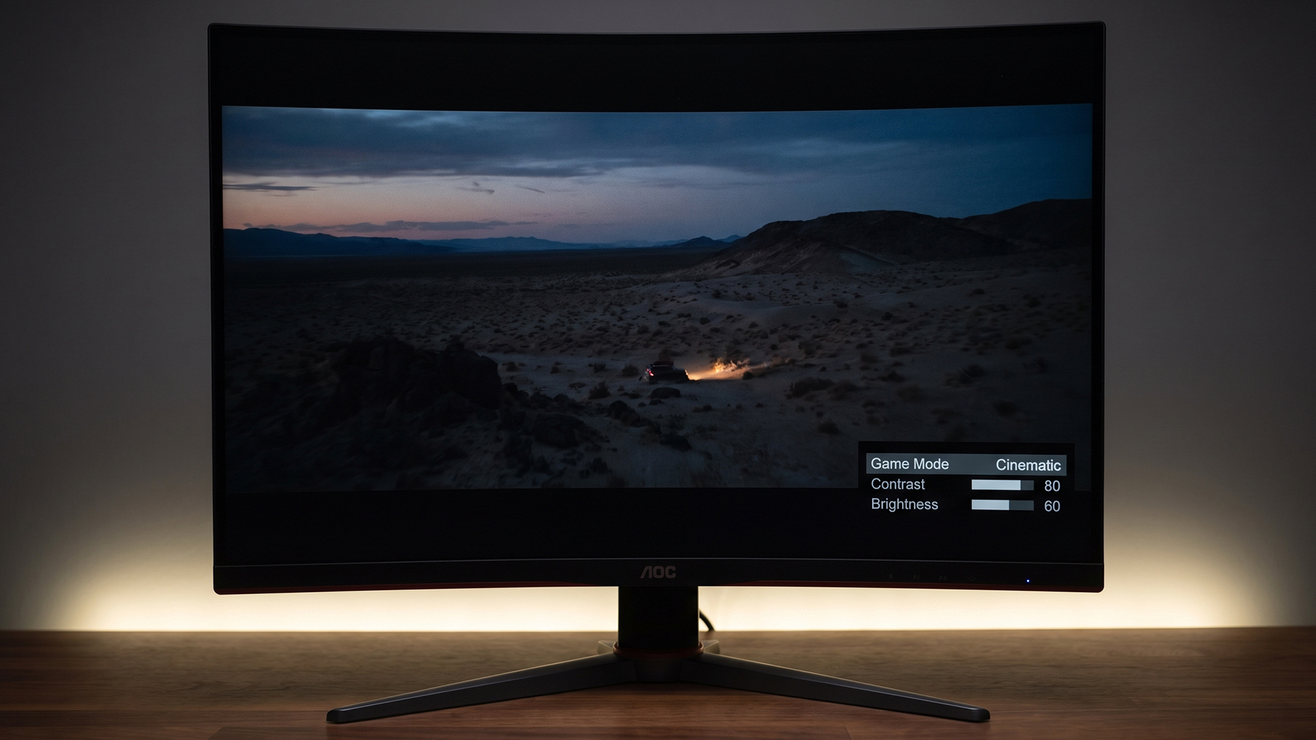 A curved AOC monitor in a dark room showing game mode settings over a cinematic landscape.
