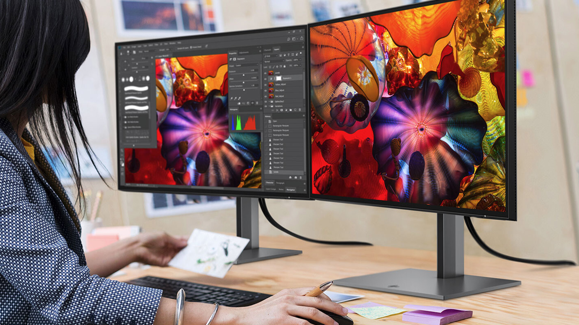 A designer working with dual IPS monitors featuring vibrant color displays on a desk.