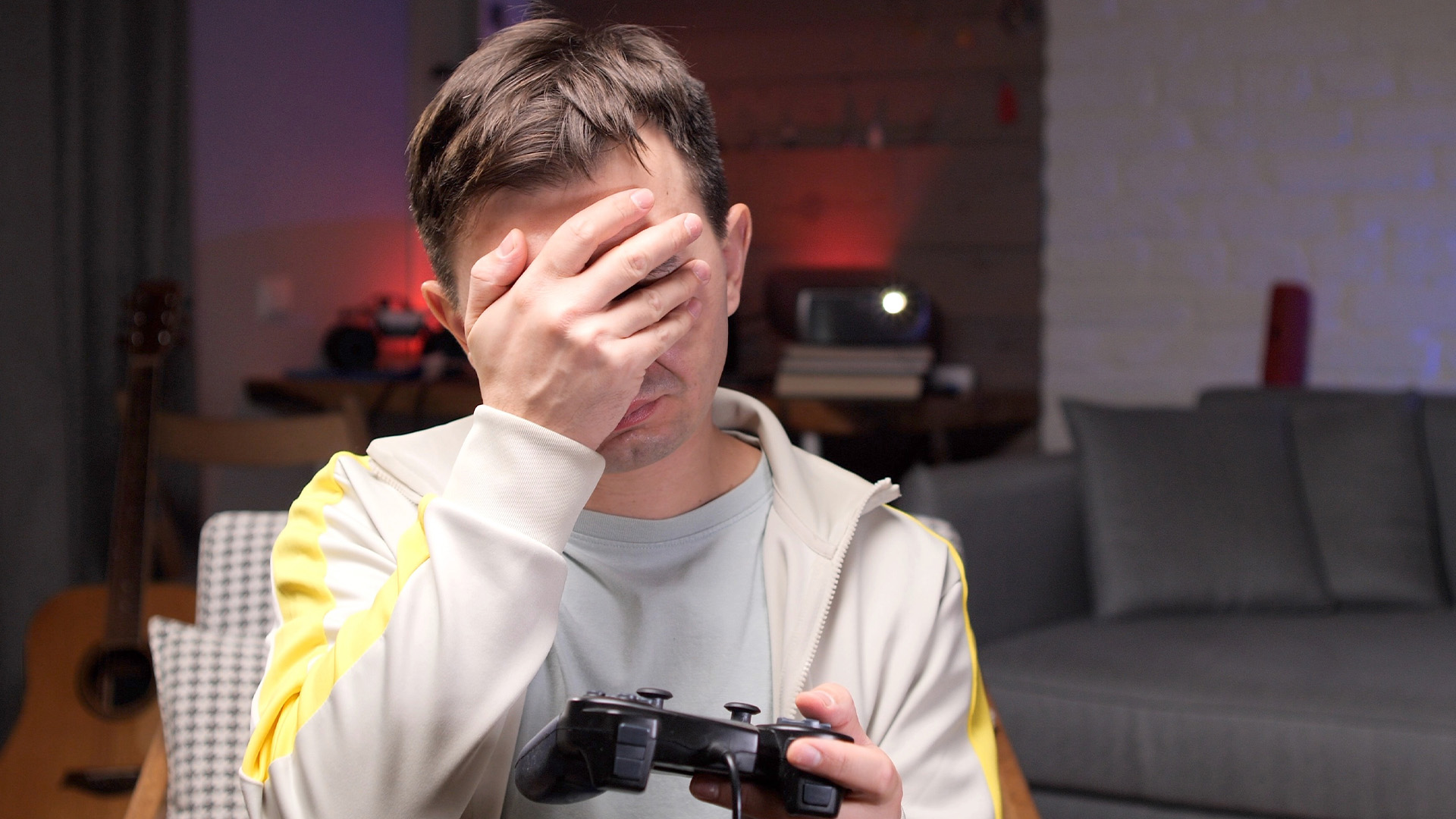 Disappointed gamer covering his face in frustration holding a controller.
