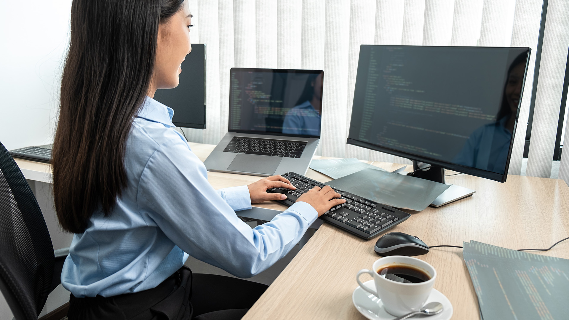 A woman working on dual screens with code displayed.