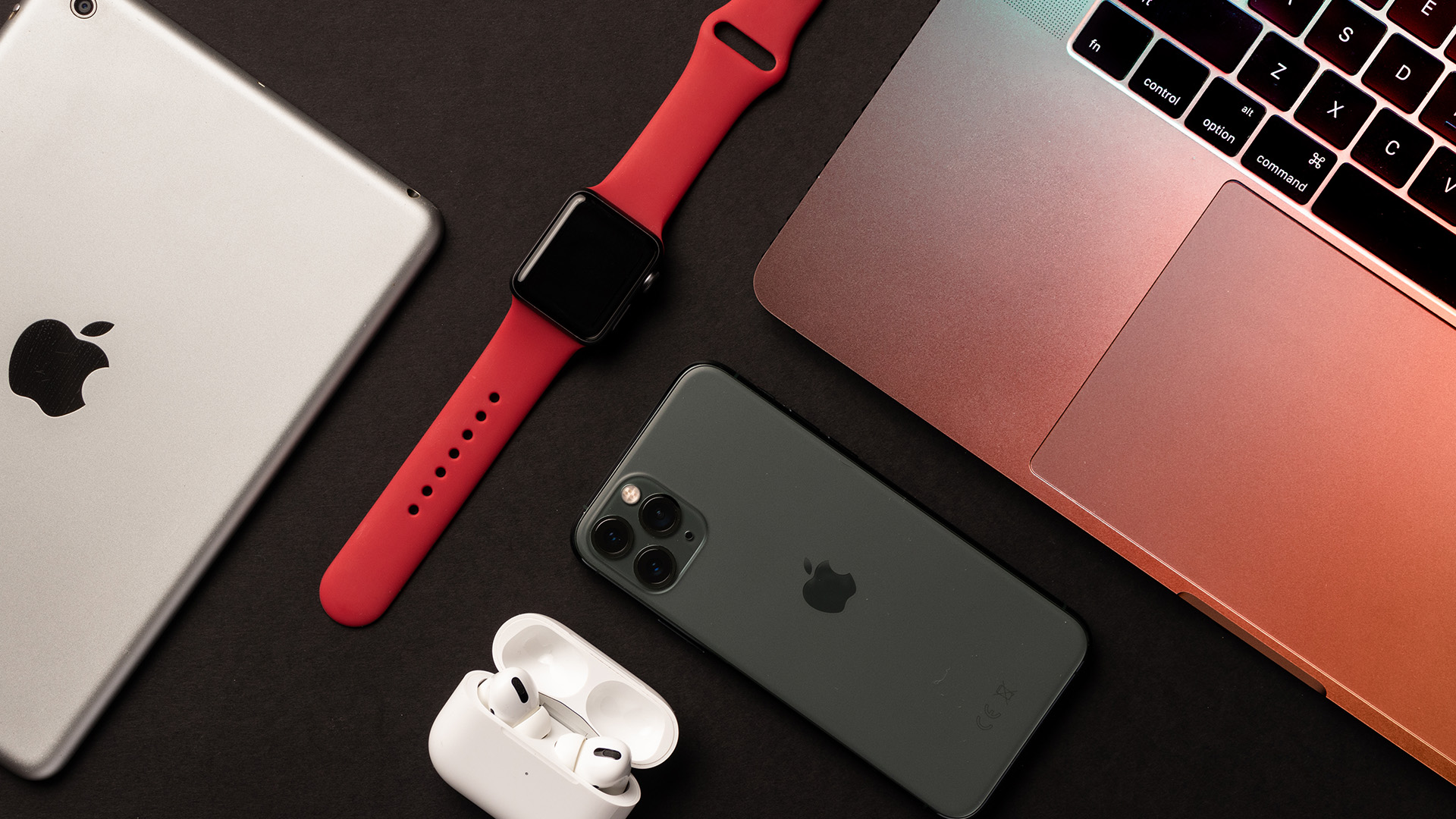 Flat lay arrangement of various Apple devices including an iPad, watch, and iPhone.