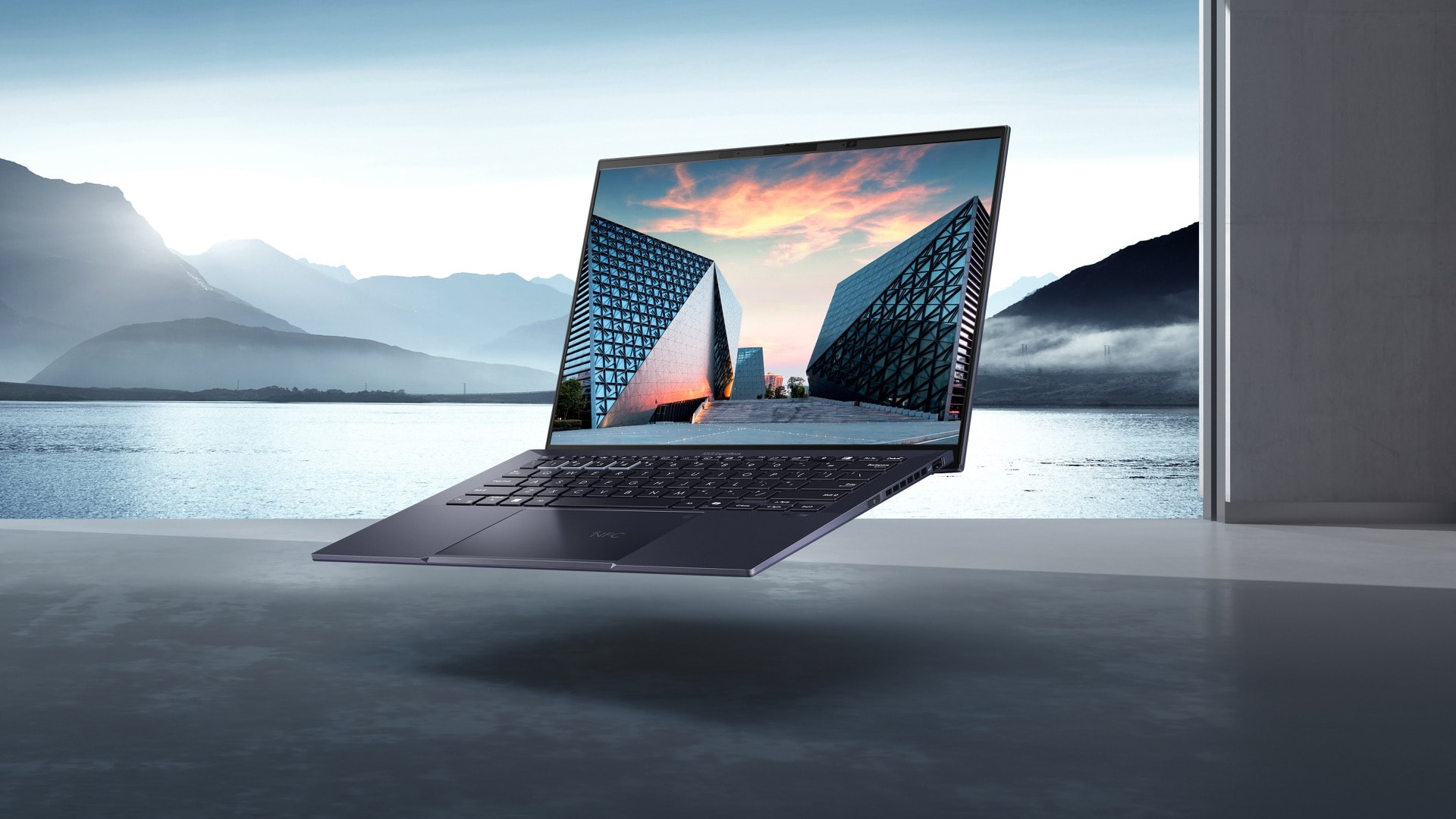 Floating OLED laptop showing a vivid architectural screen against a landscape.