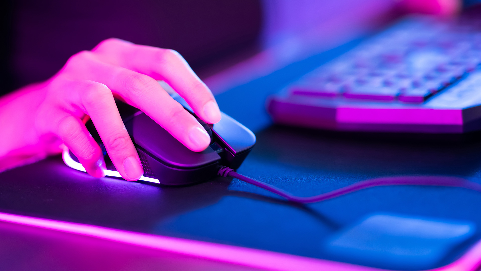 Gamer's hand using a mouse with RGB lighting on a mousepad.