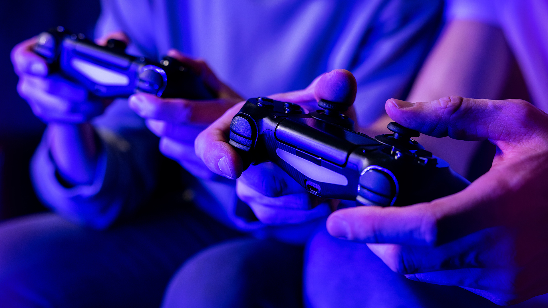 Two gamers holding wireless controllers during a multiplayer session under neon lighting.