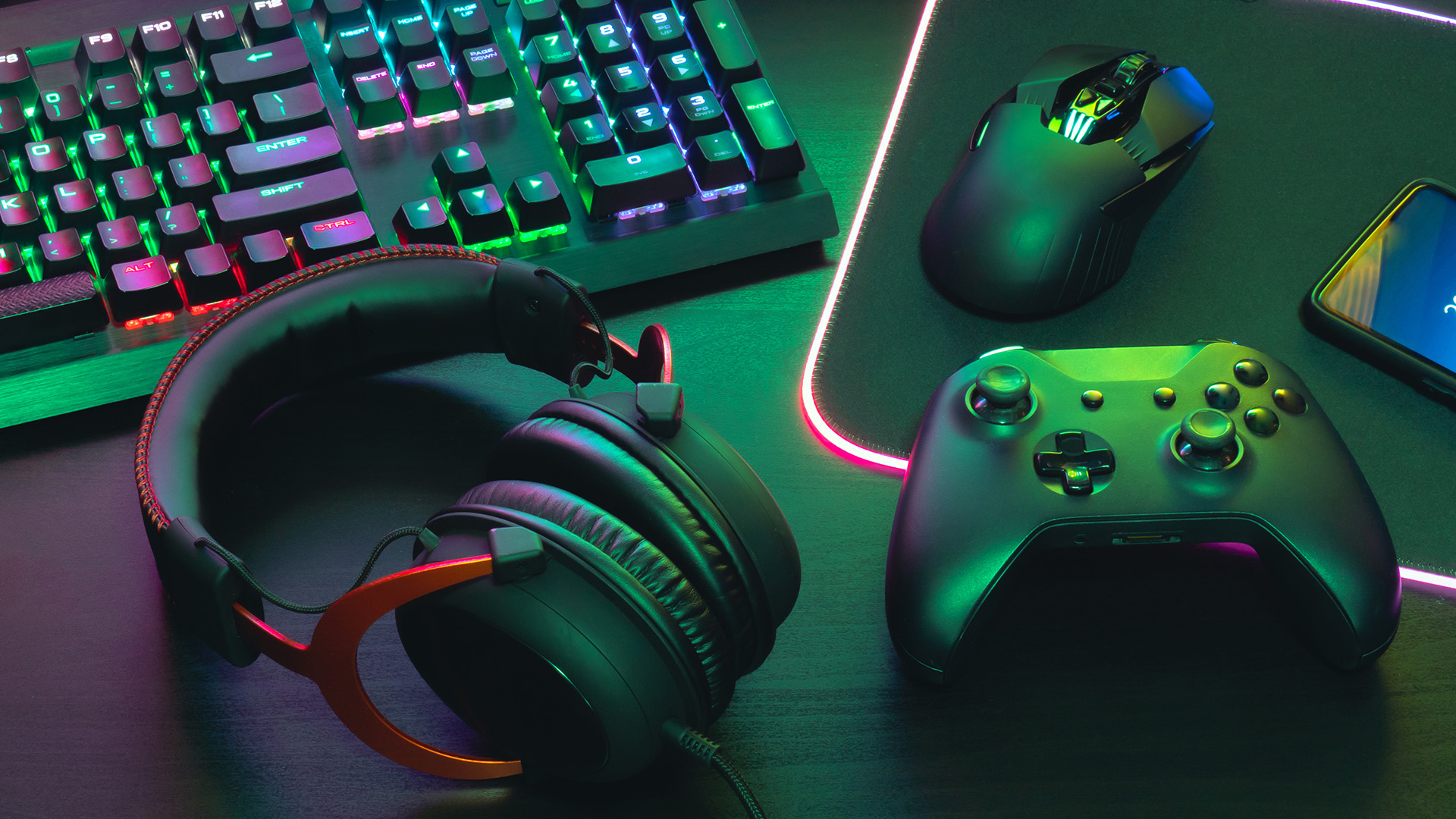 A gaming headset, wireless controller, and mouse arranged next to an RGB keyboard.