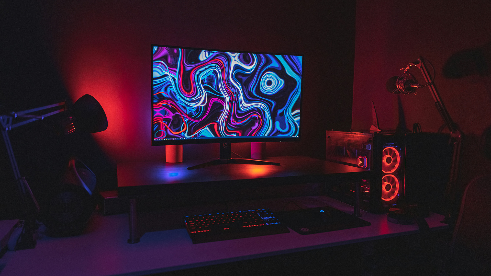 A gaming PC setup featuring a monitor with a colorful abstract background and red ambient lighting.