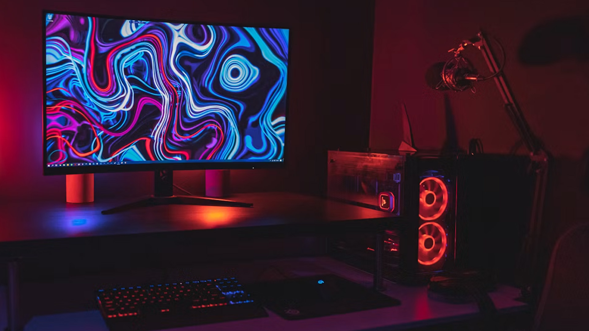A gaming PC setup featuring a curved monitor displaying an abstract colourful wallpaper and red ambient case lighting.