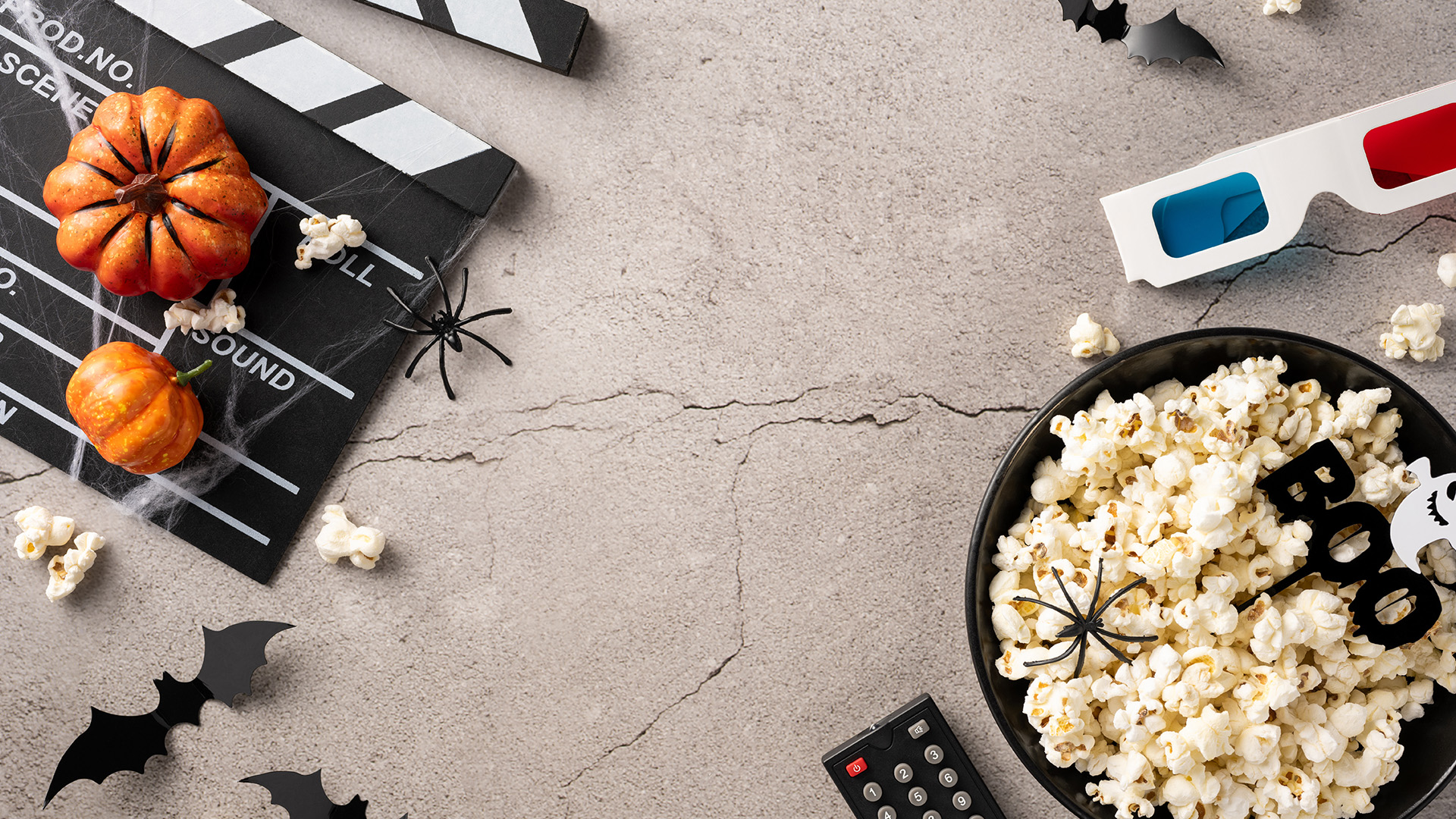 A flat lay arrangement of Halloween movie night essentials including popcorn, film clapperboard, mini pumpkins, and spiders.