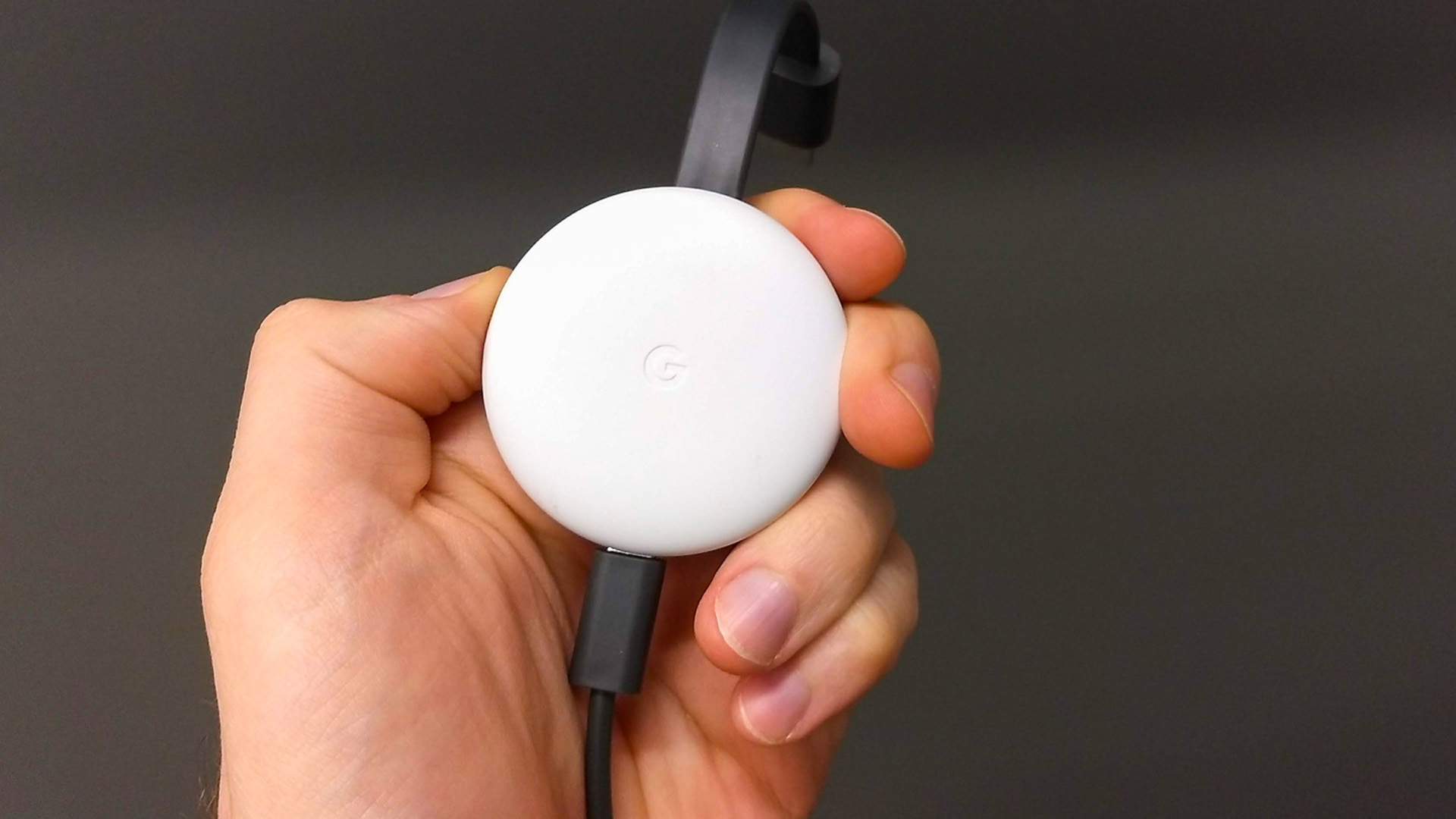 Close-up of a hand holding a white Chromecast streaming device with cable.