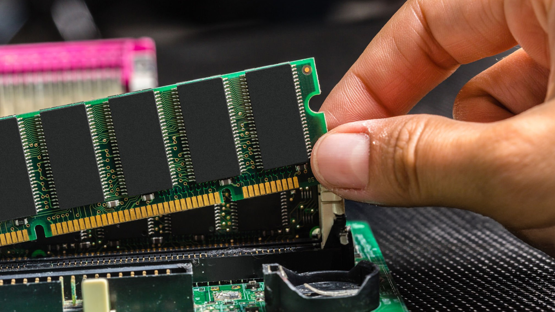 A close-up of a hand carefully inserting a RAM stick into a motherboard.