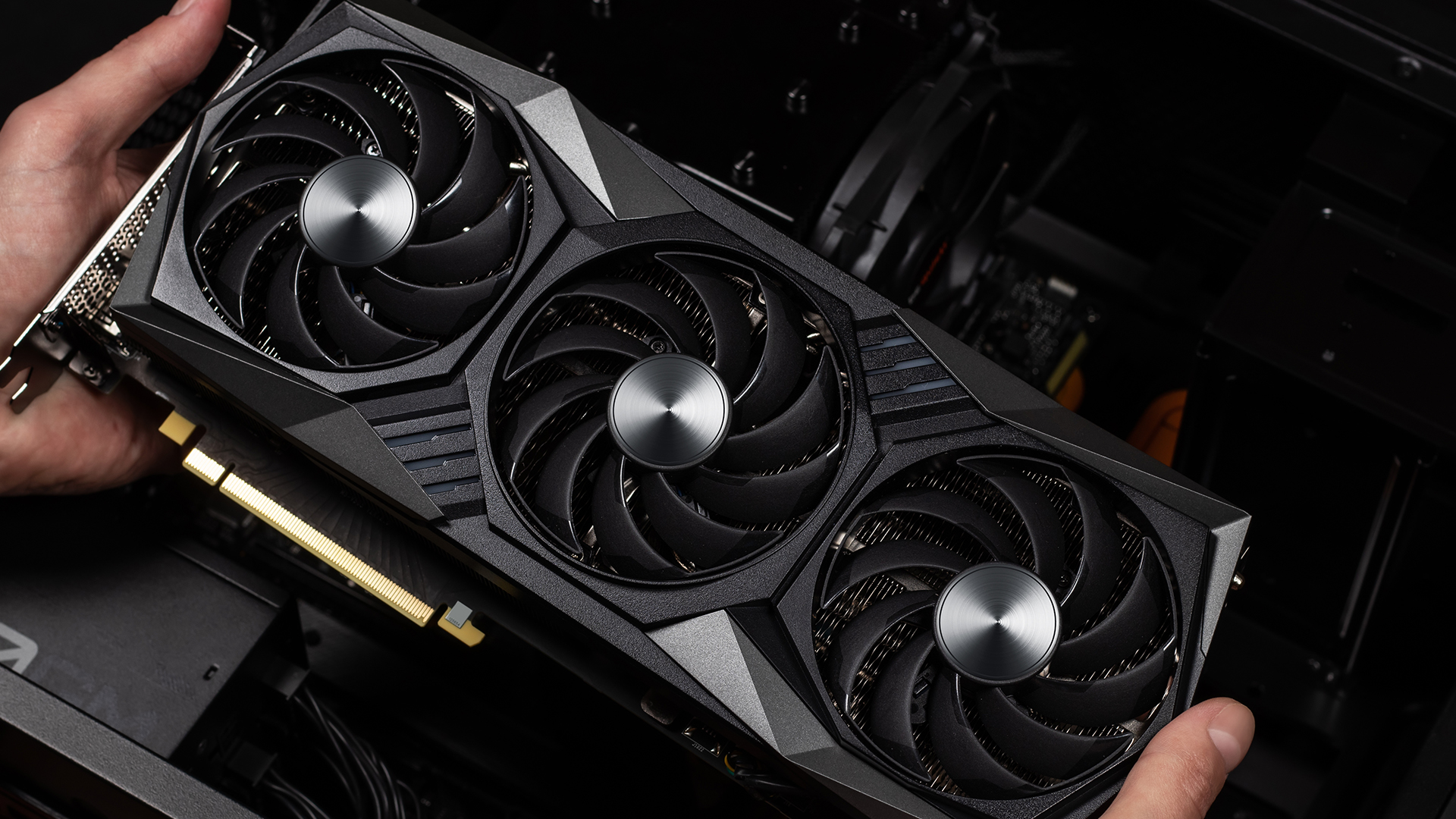 Hands holding a modern triple-fan graphics card inside a black PC chassis.