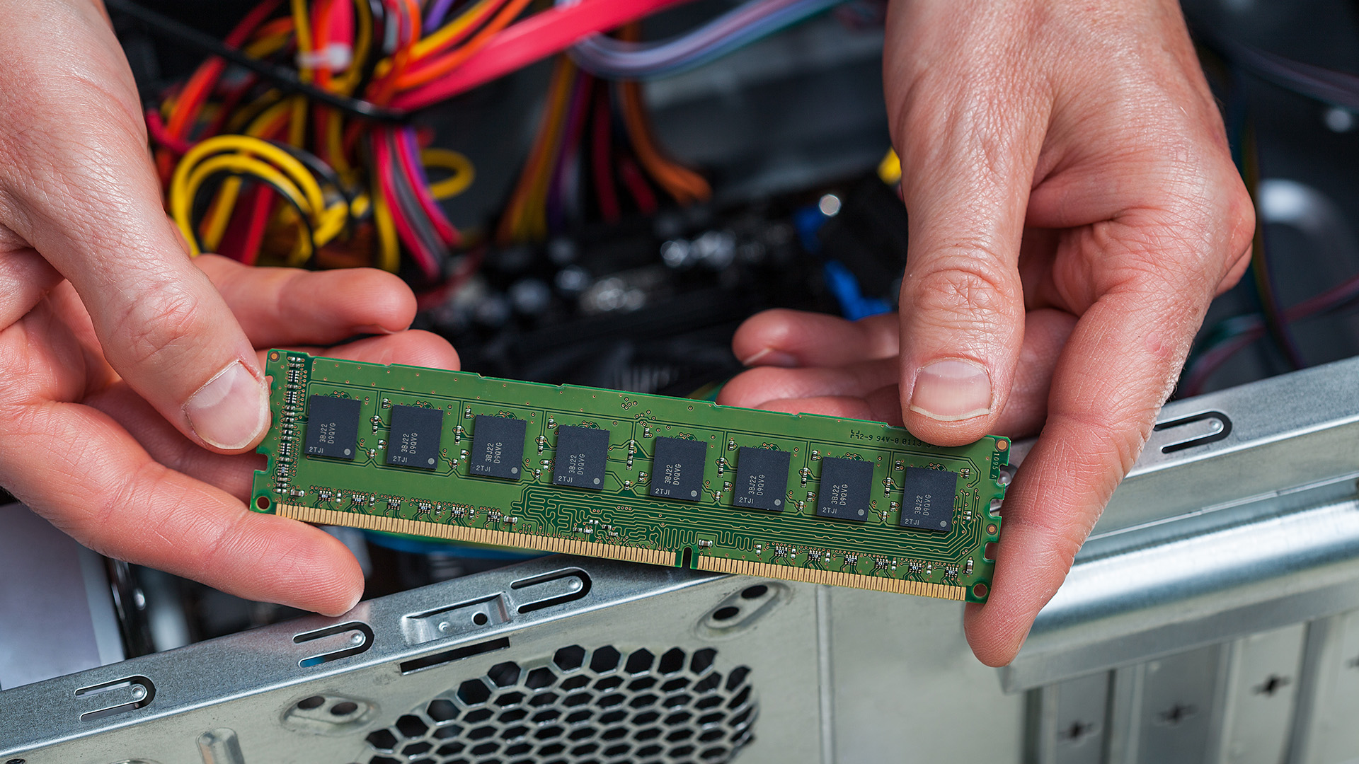 Two hands holding a green RAM module over an open desktop PC case.