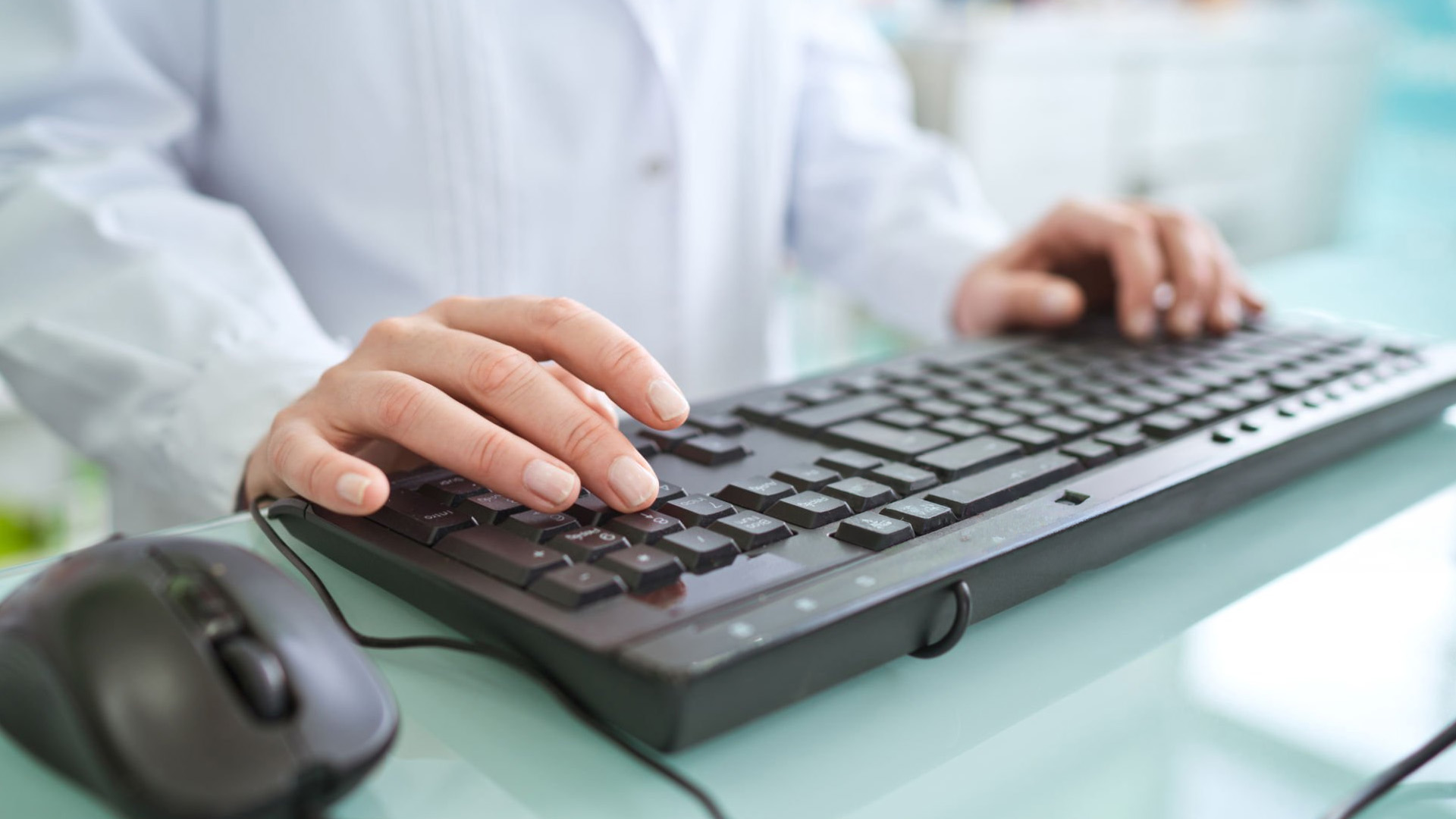 Professional typing on a black keyboard with a mouse nearby.