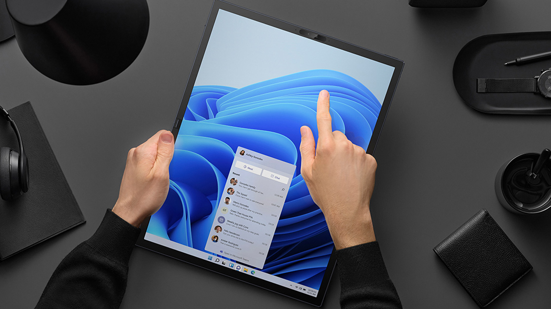 Hands of a person interacting with a foldable laptop touchscreen on a desk.