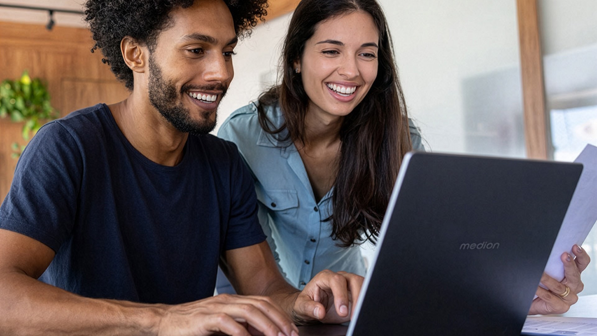 Smiling man and woman looking together at a black Medion laptop screen.