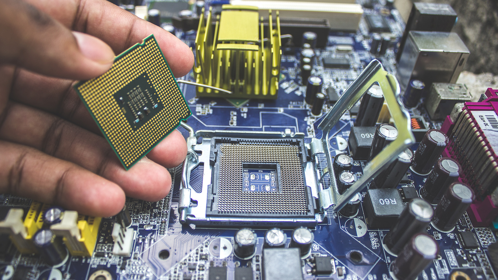 A person holding a processor above a motherboard socket prior to installation.