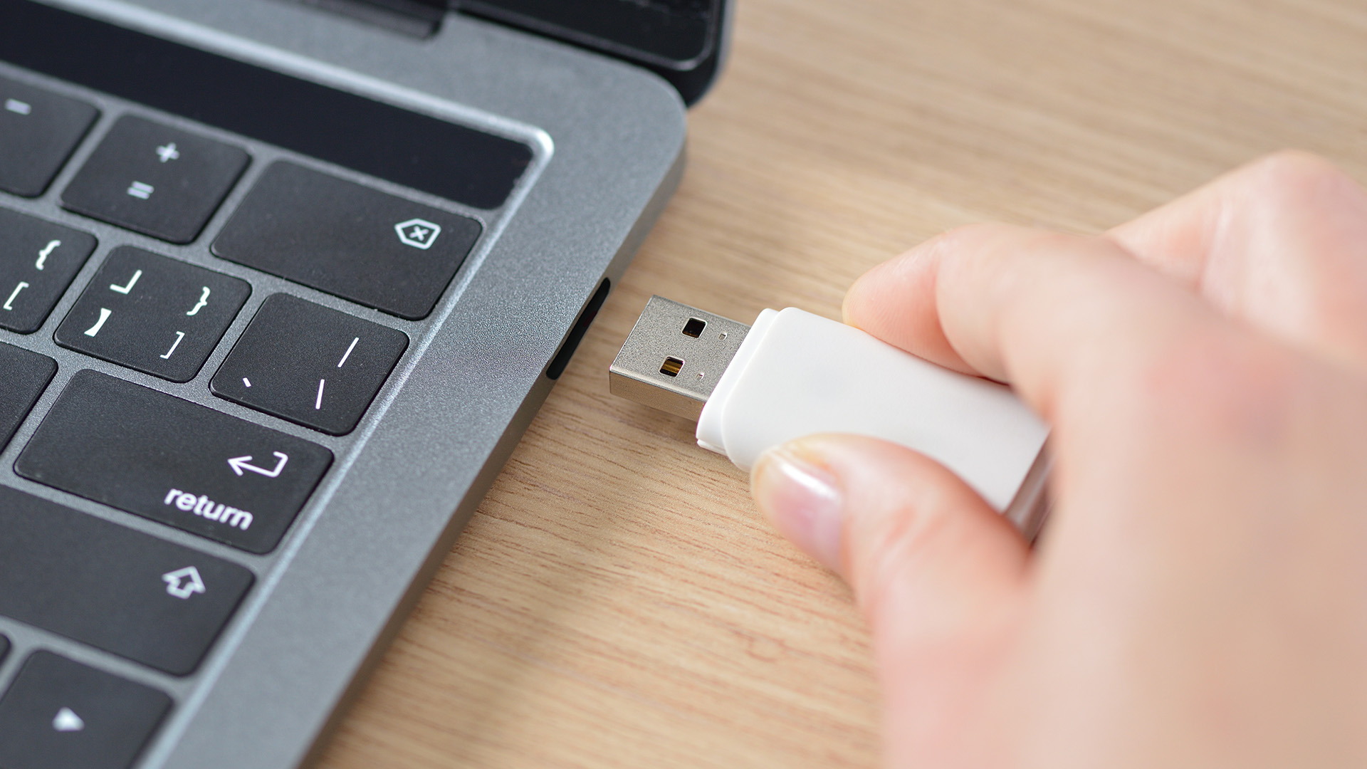 A person inserting a white USB flash drive into the side port of a laptop.