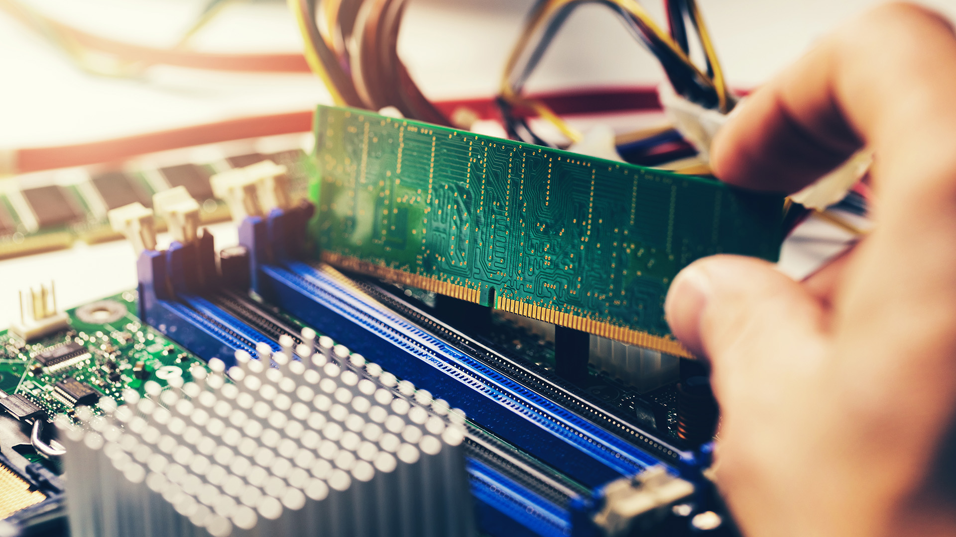 Close-up of a hand inserting a green RAM module into a motherboard slot.