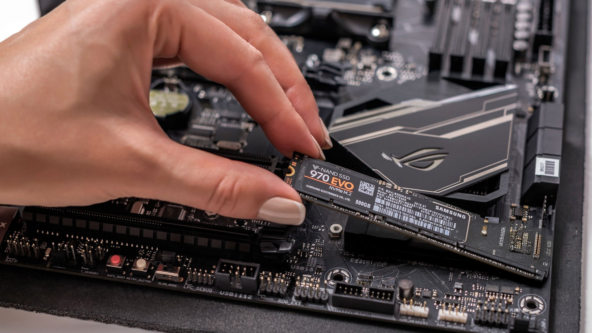 A hand inserting a Samsung 970 EVO NVMe SSD into a desktop PC motherboard.
