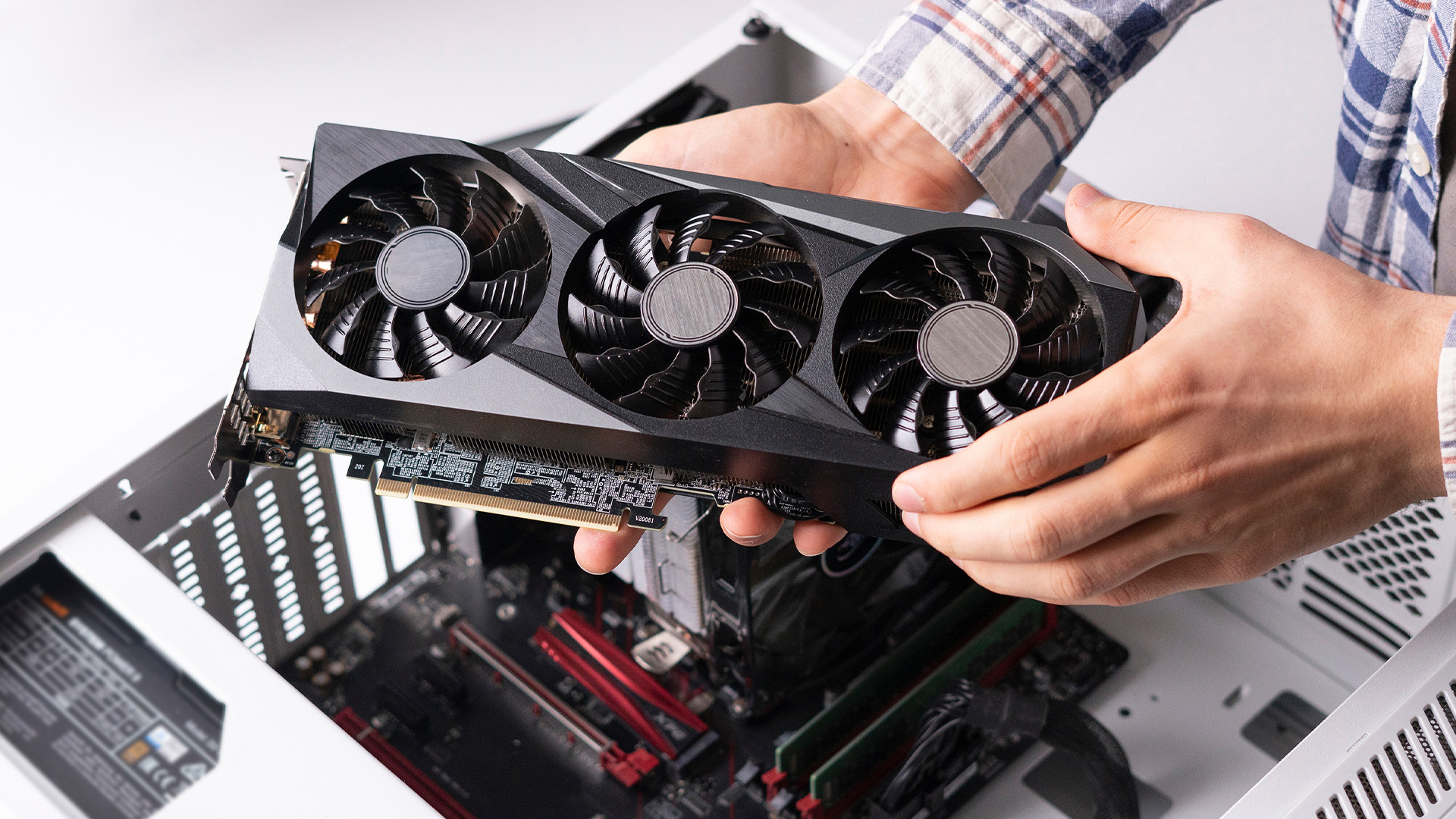 A PC builder holding a triple-fan graphics card over an open desktop case, preparing for installation.