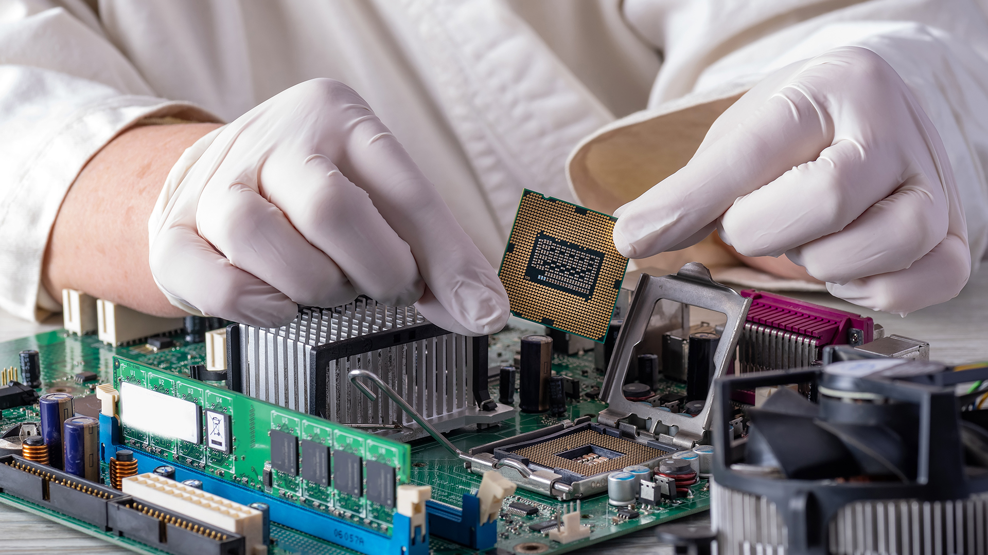 Hands in gloves installing a CPU into a motherboard socket.