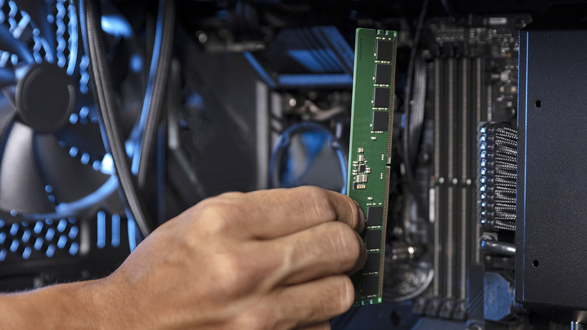 A hand holding a green RAM stick vertically inside a dark desktop PC chassis.