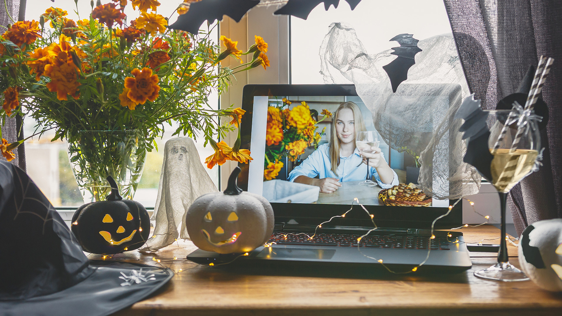 A laptop showing a video call surrounded by Halloween decorations and pumpkins.
