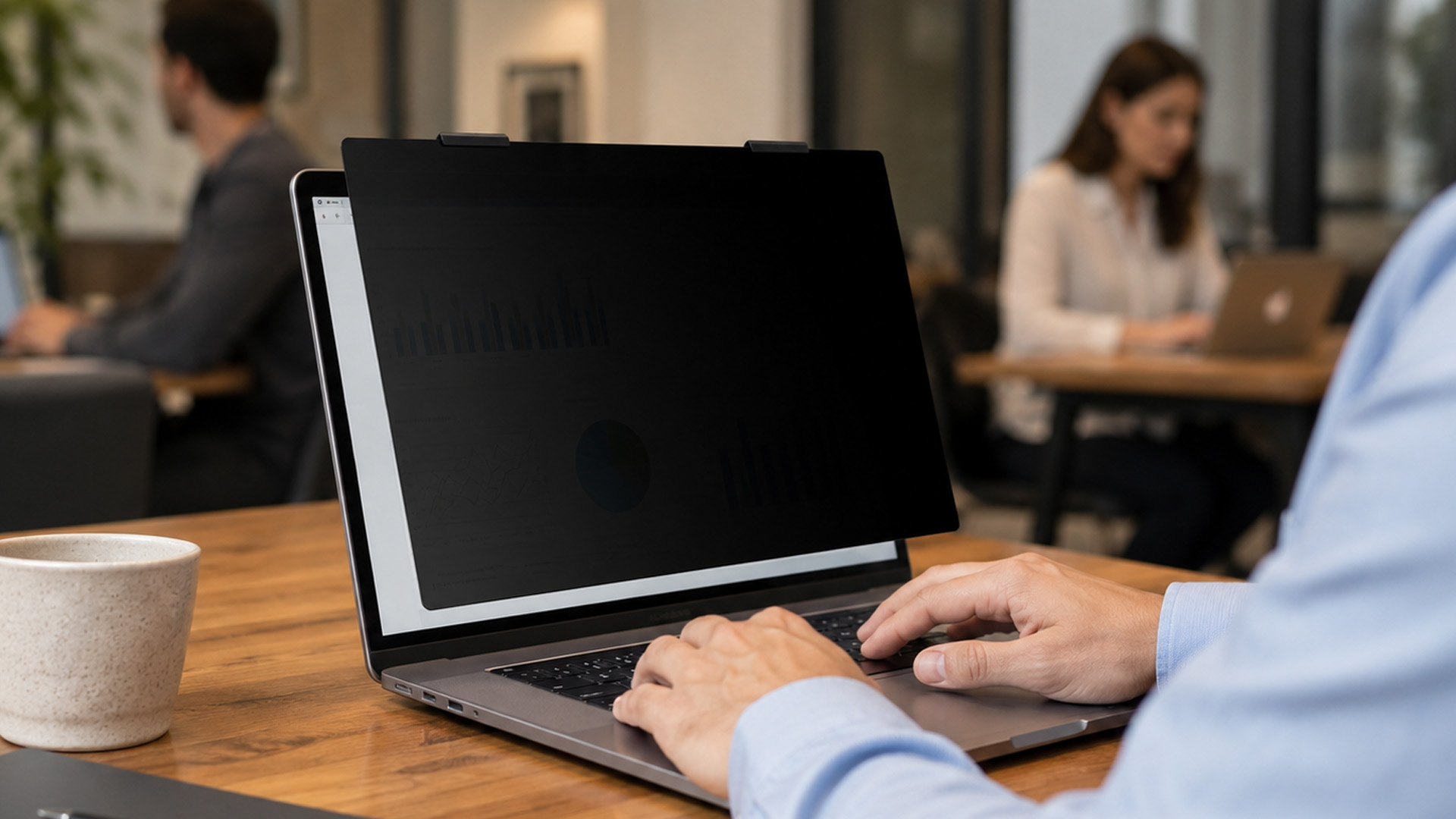 Man working on a laptop with a clip-on privacy screen filter attached in an office environment.