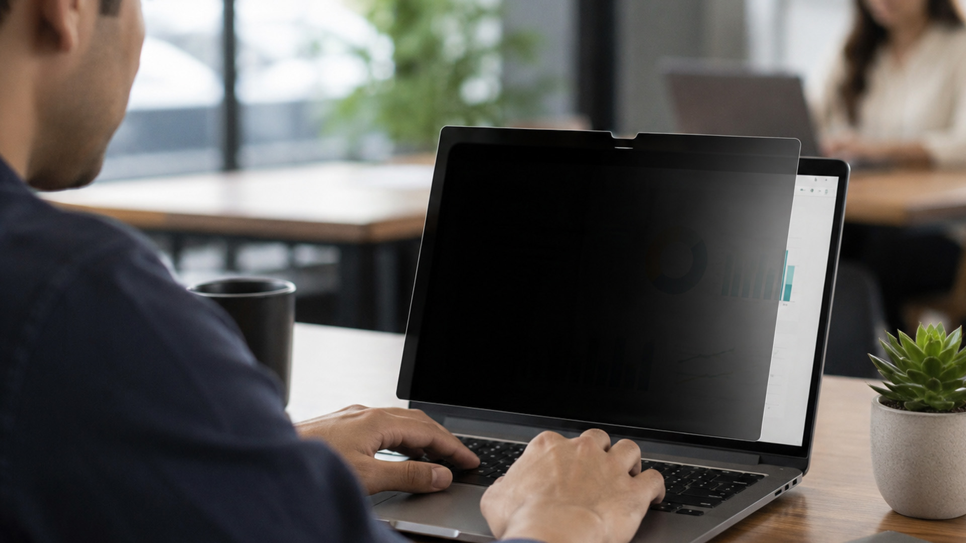 Side-angle view of a person using a laptop with a privacy screen protector darkening the display.