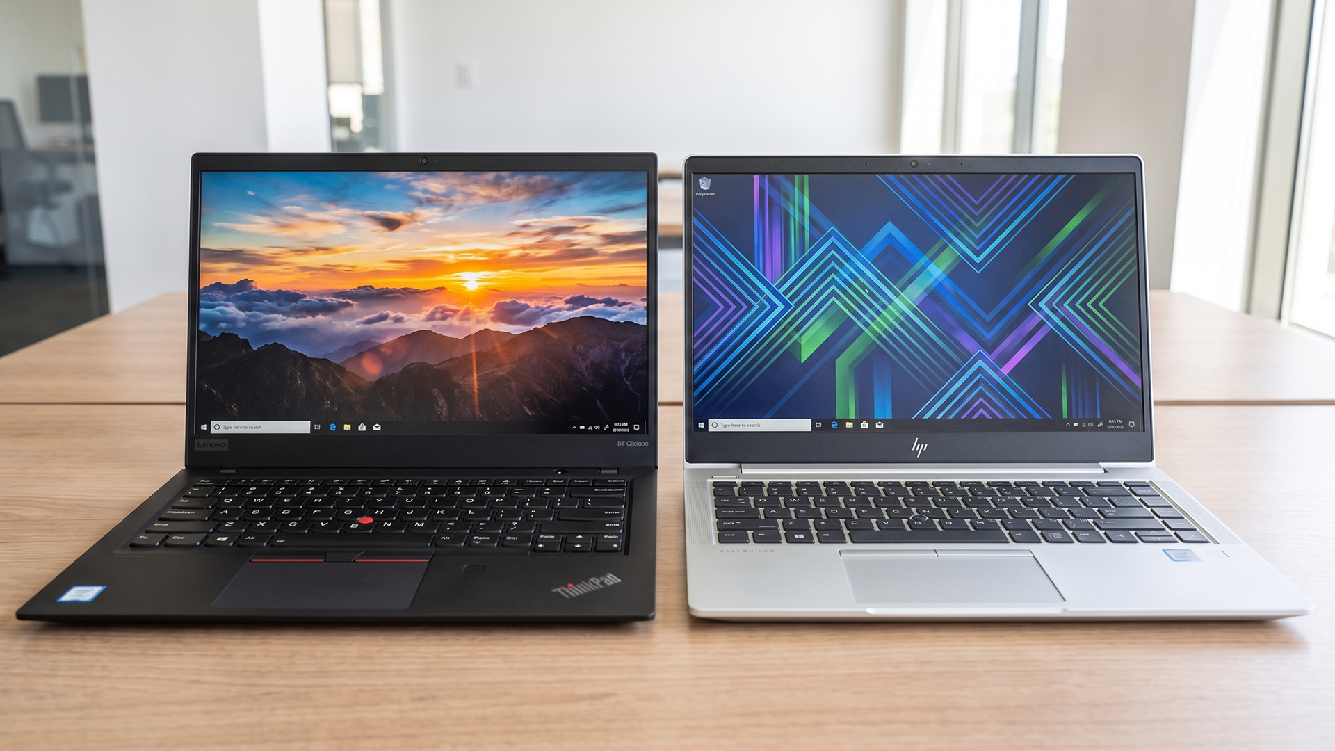 Black Lenovo ThinkPad and silver HP EliteBook laptops side by side on a desk.