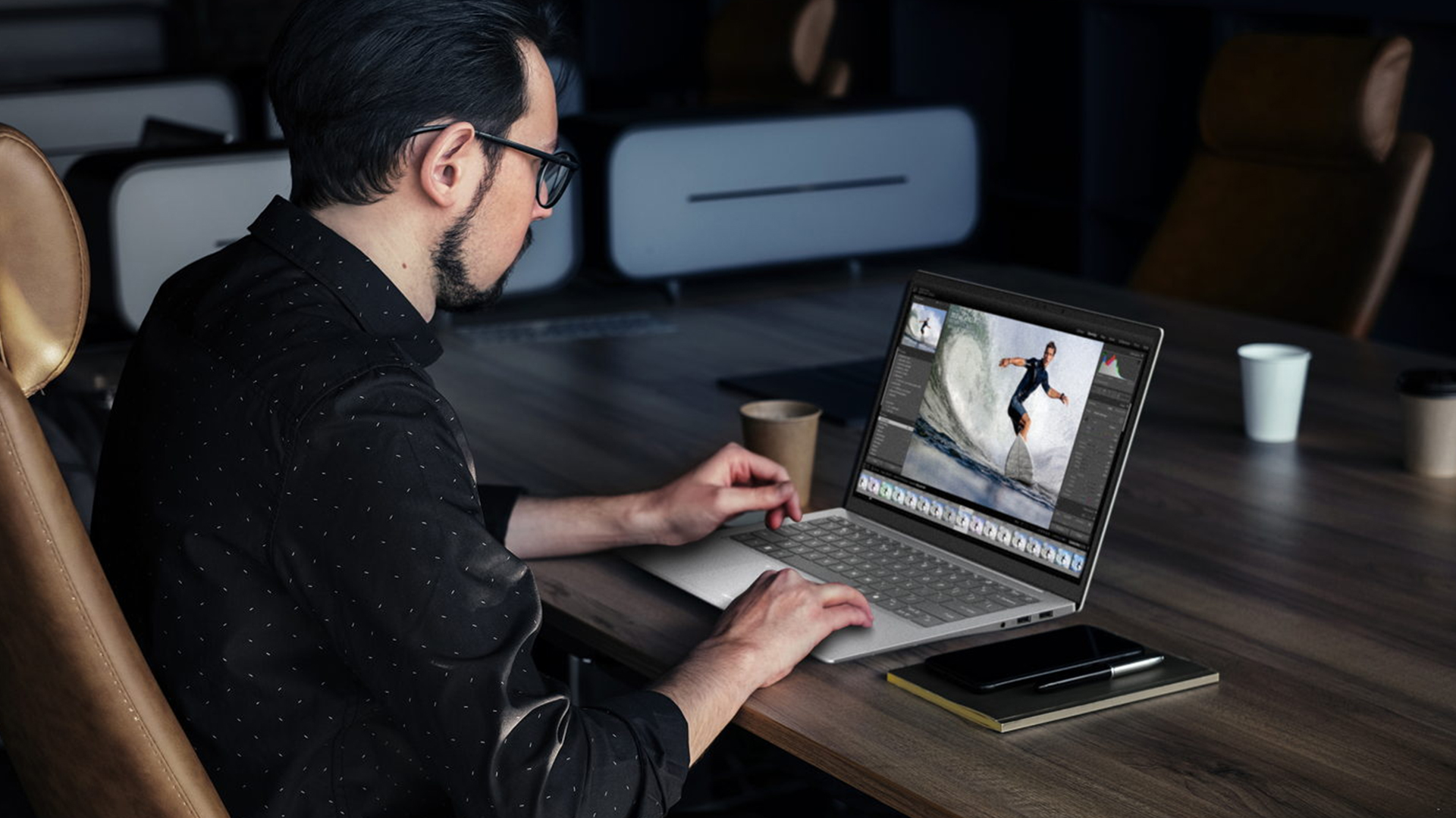 Man editing a surfing photo on a laptop at a conference table.