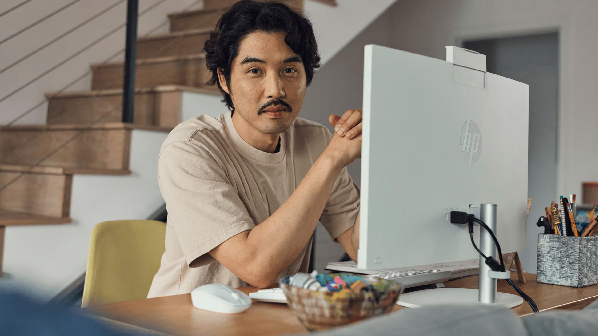 A man sitting at a wooden desk next to a white all-in-one PC setup.