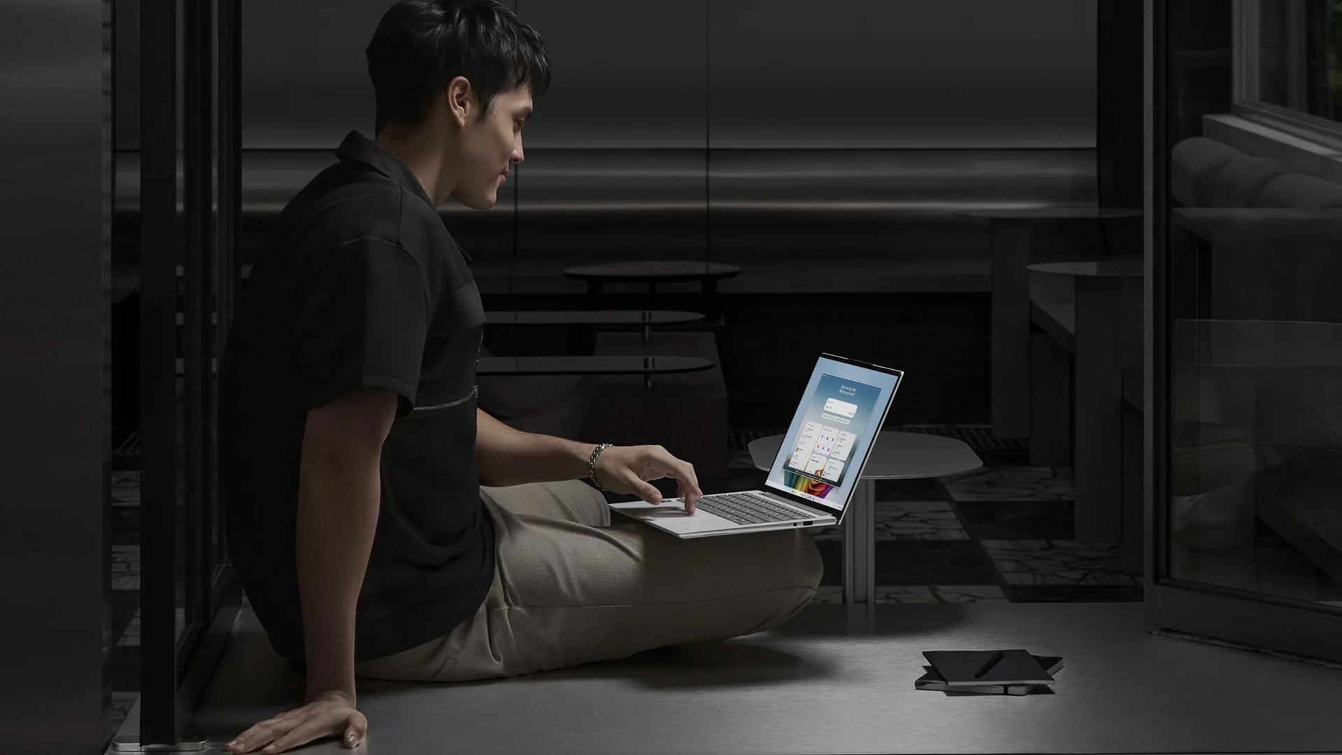 Man sitting on the floor in a dark room using the touchpad on a silver Acer laptop.