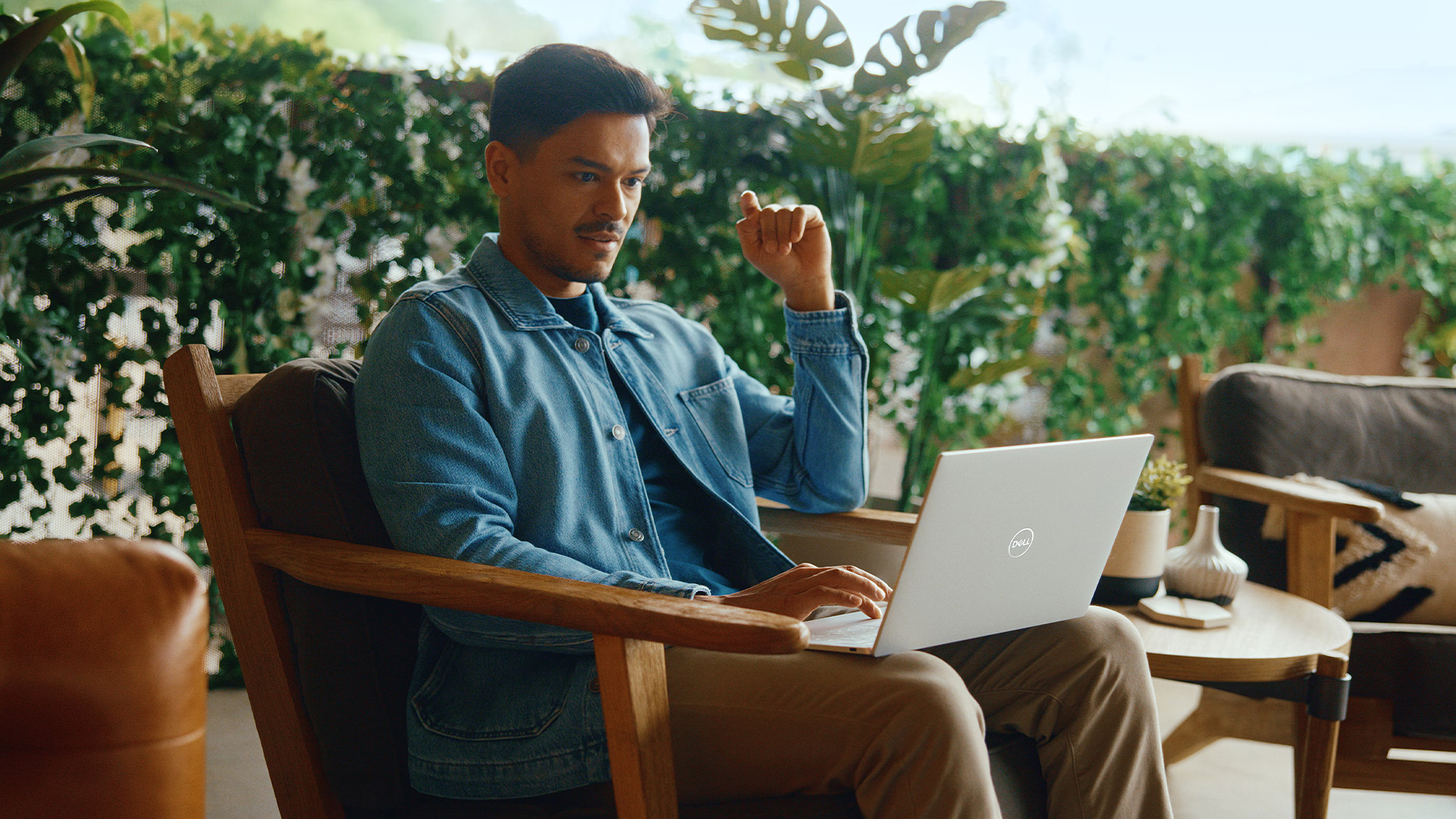 Man sitting on an outdoor patio armchair using a silver Dell laptop.