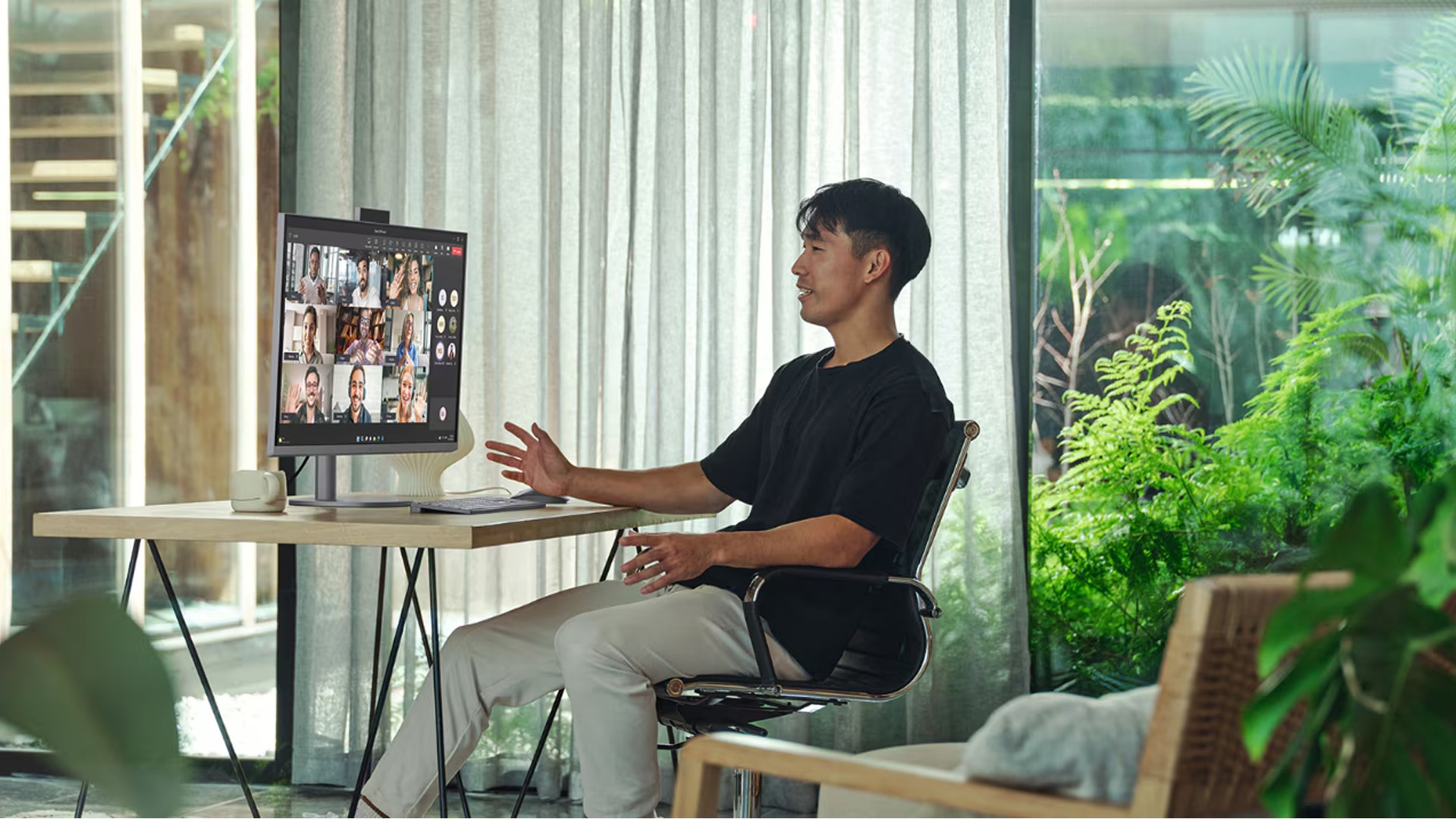 A man working on an all-in-one computer during a video call in a bright office.