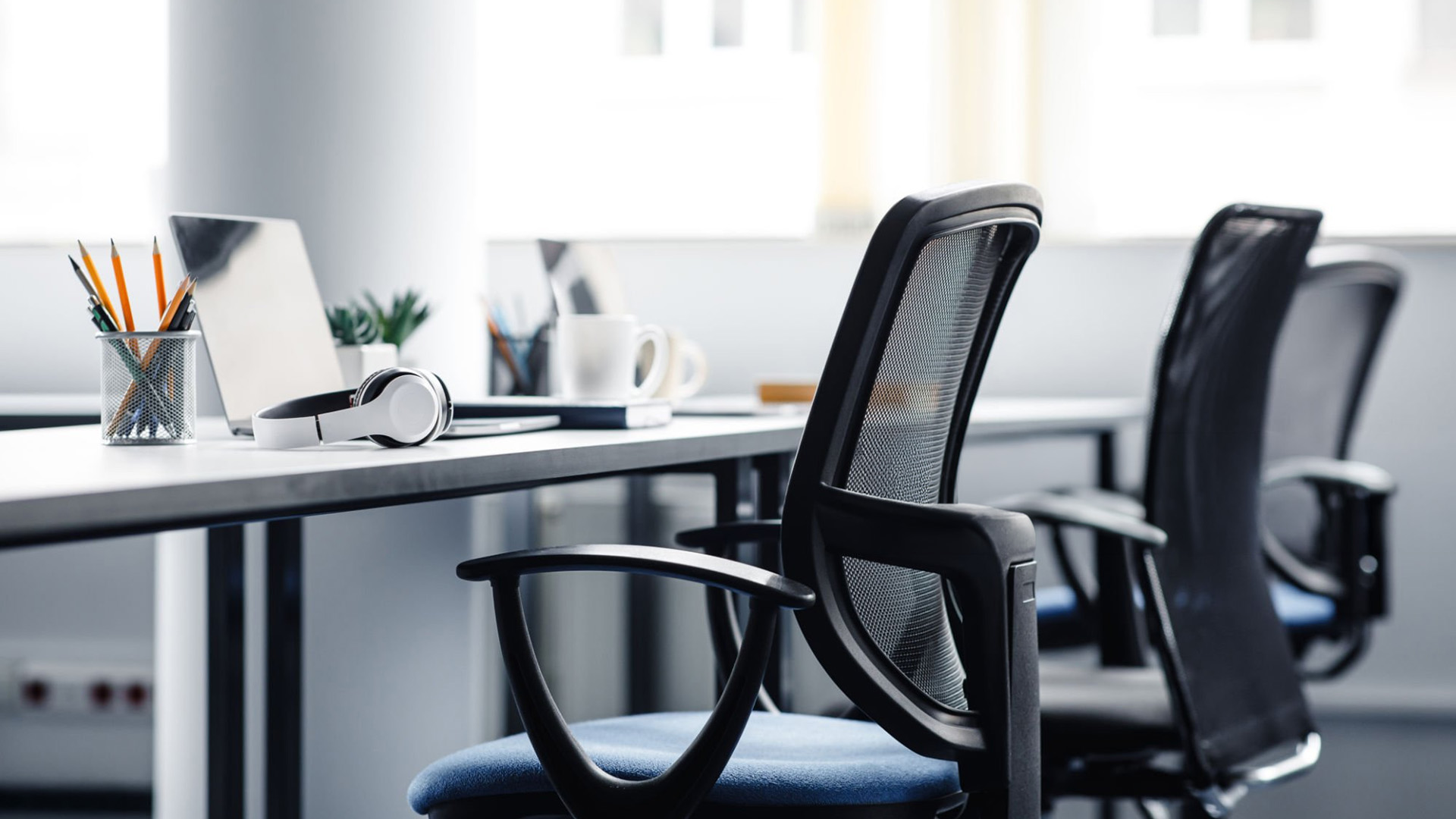 Black mesh office chairs at a white desk in a bright, modern office space.