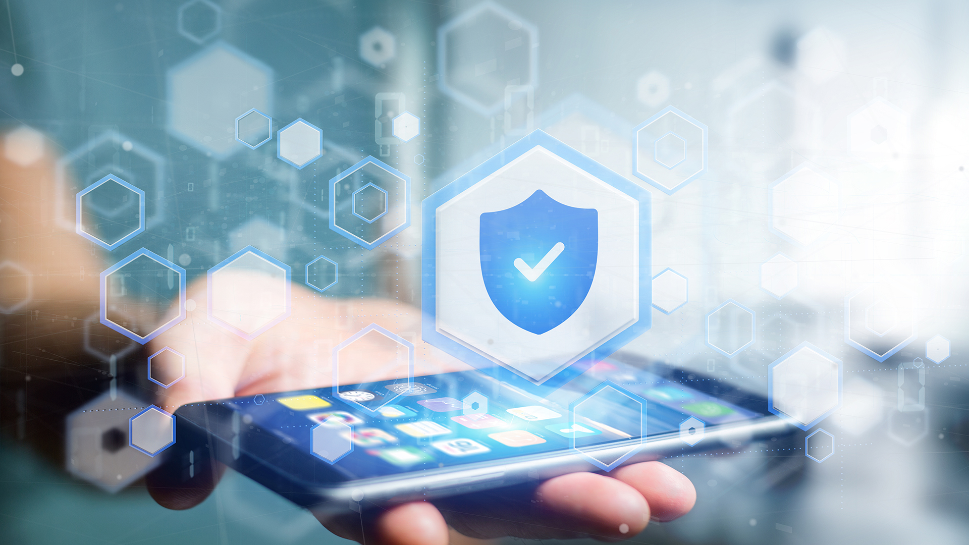 Hands holding a smartphone featuring a glowing blue cybersecurity shield protection interface.