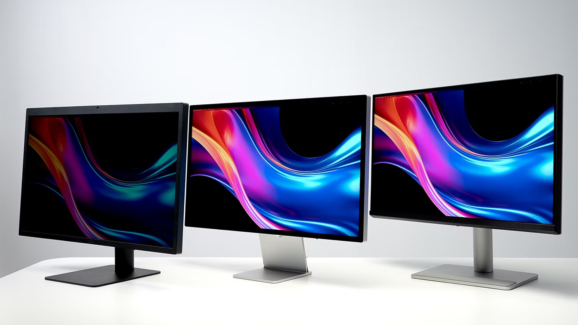 Three computer monitors lined up showcasing colourful abstract wallpapers.