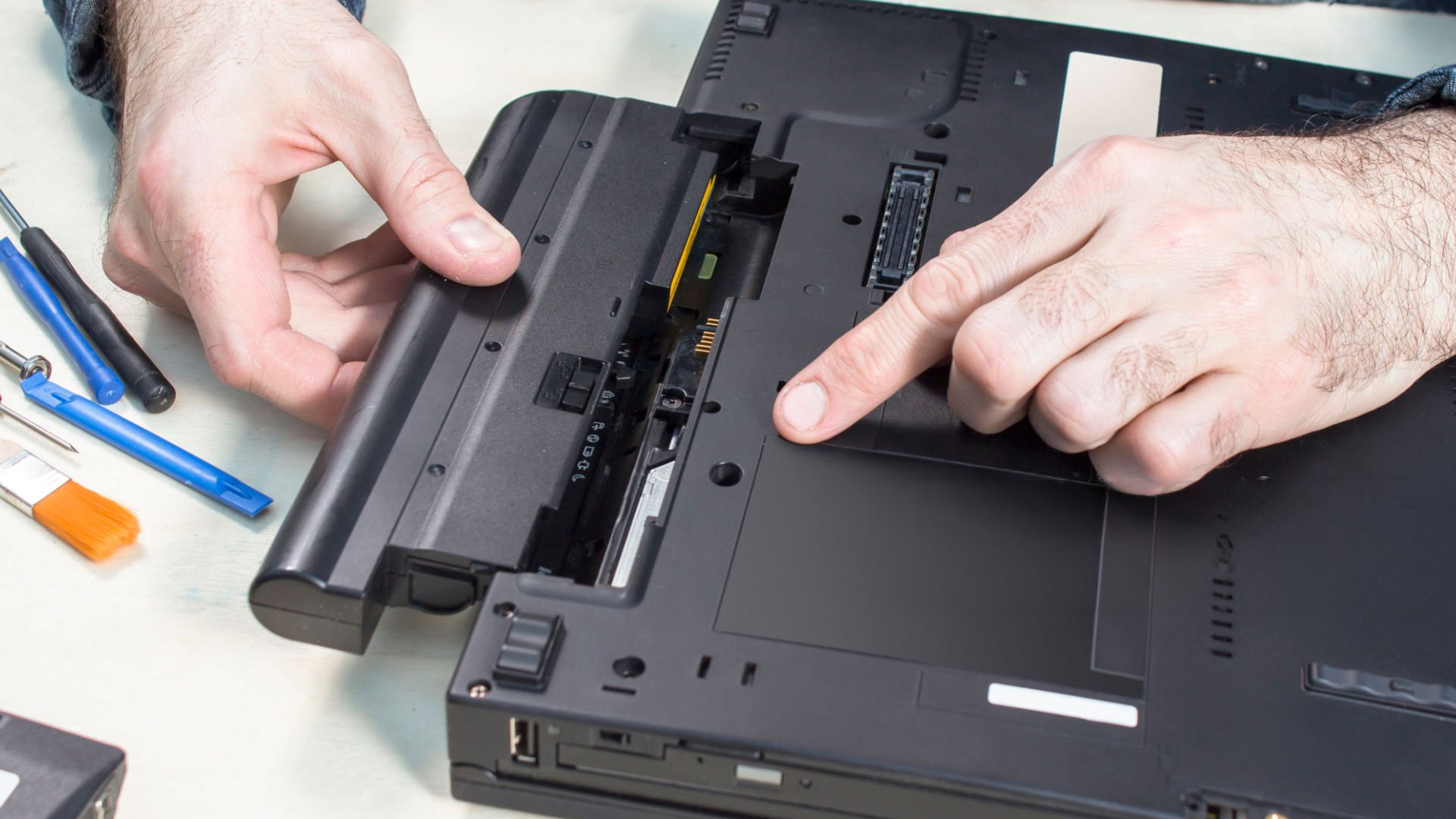 Hands inserting a removable battery into the compartment of a laptop computer.